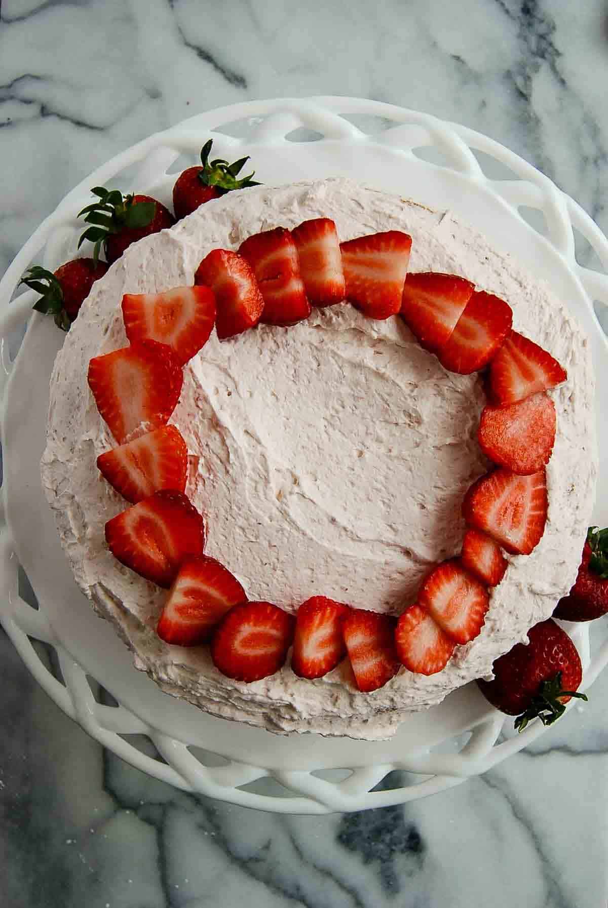 closeup of strawberry vanilla cake with strawberry whipped cream icing and fresh, sliced strawberries on top.