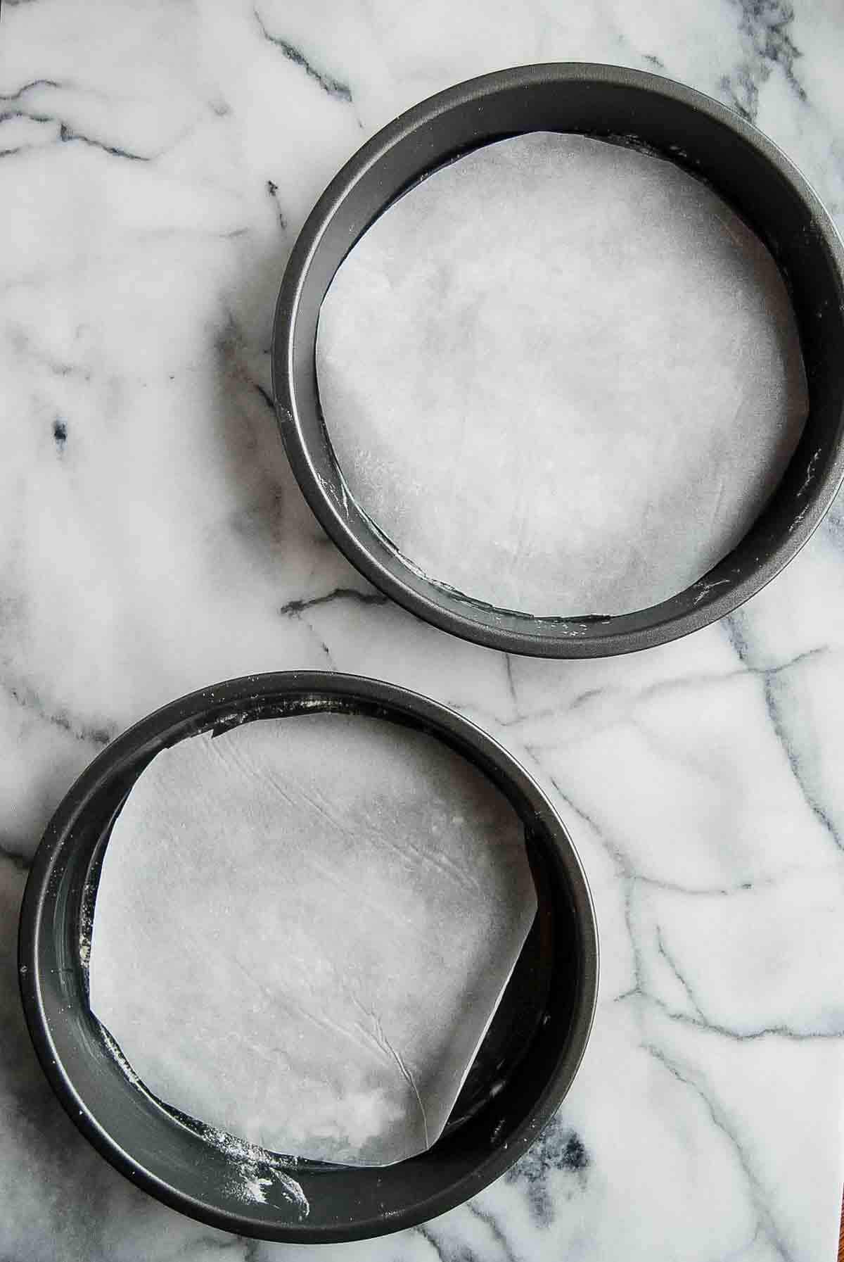 two round cake pans with parchment paper on the bottom sitting on countertop.