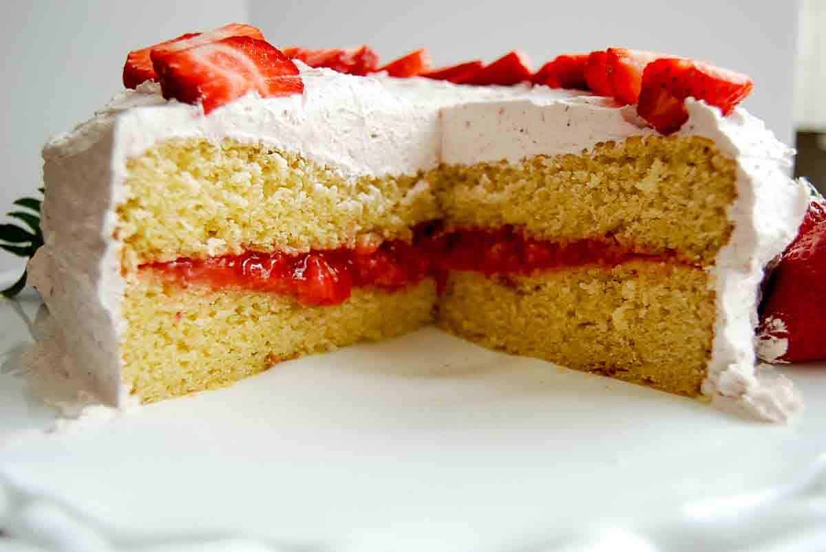 Side view of strawberry vanilla cake, with a portion cut open to see the inner strawberry cake filling.