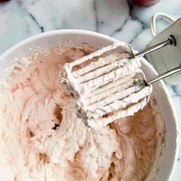 strawberry whipped cream in bowl with hand mixer to the side.