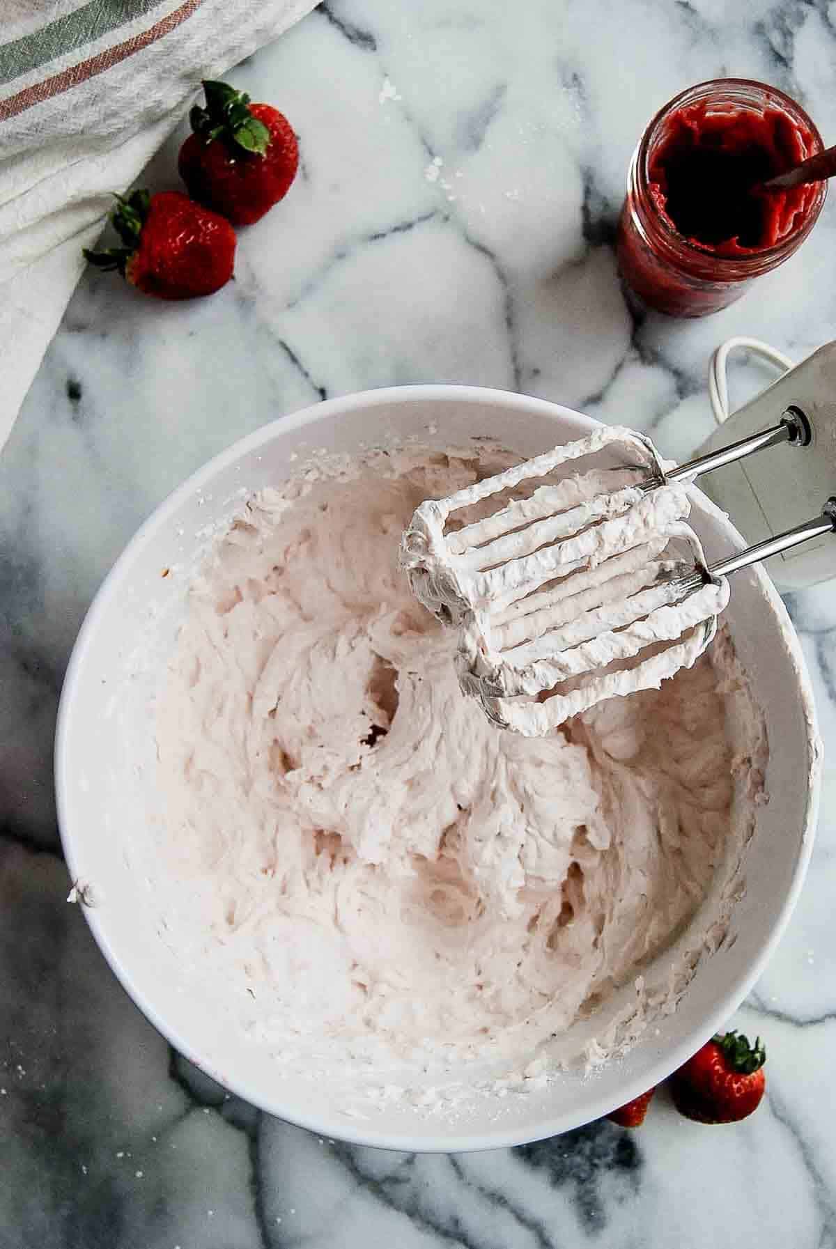 strawberry whipped cream frosting in bowl with mixer to the side.