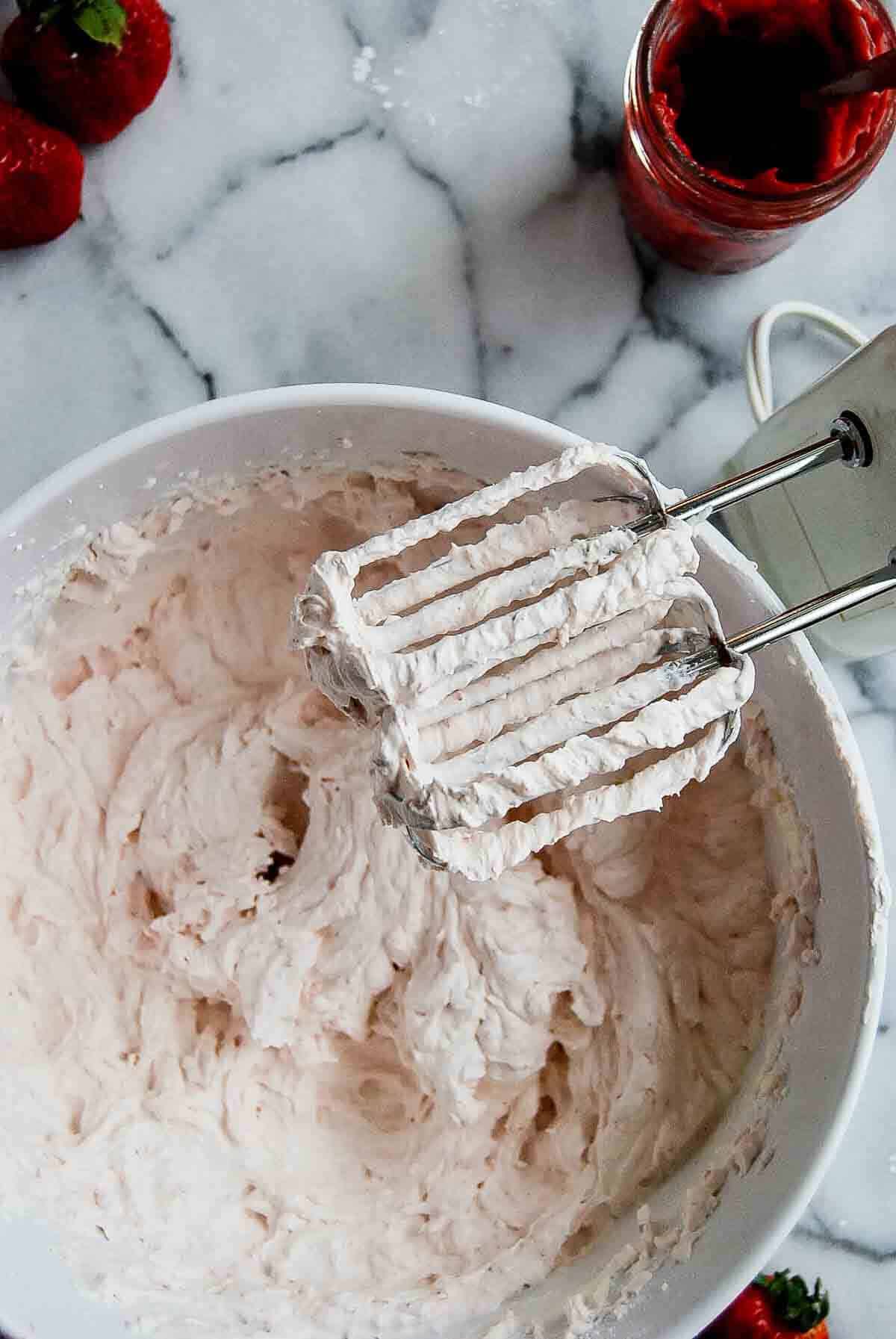 closeup of strawberry whipped cream frosting with hand mixer on the side.