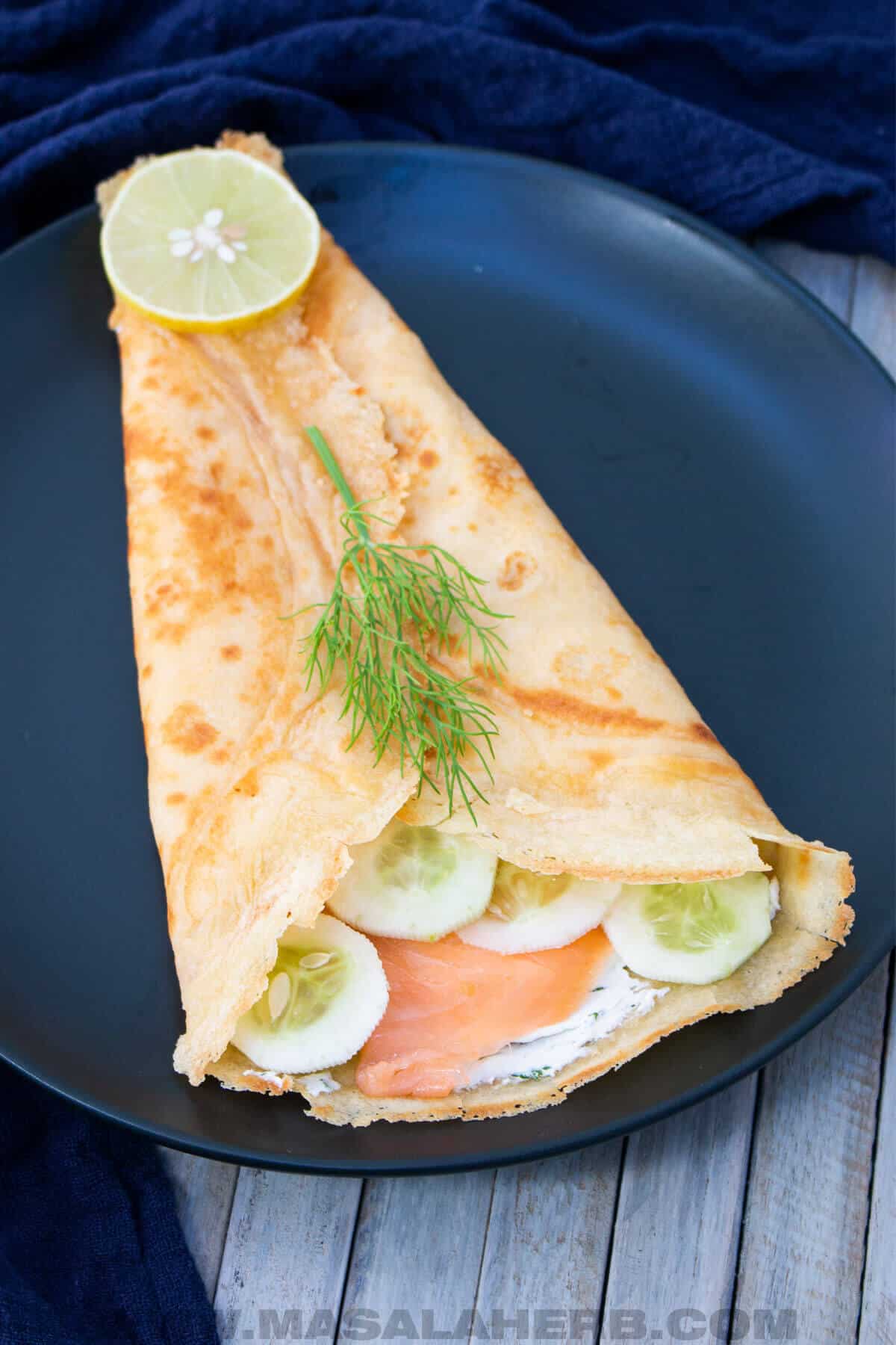 filled crepe with cream cheese, salmon, dill and cucumber on a plate.