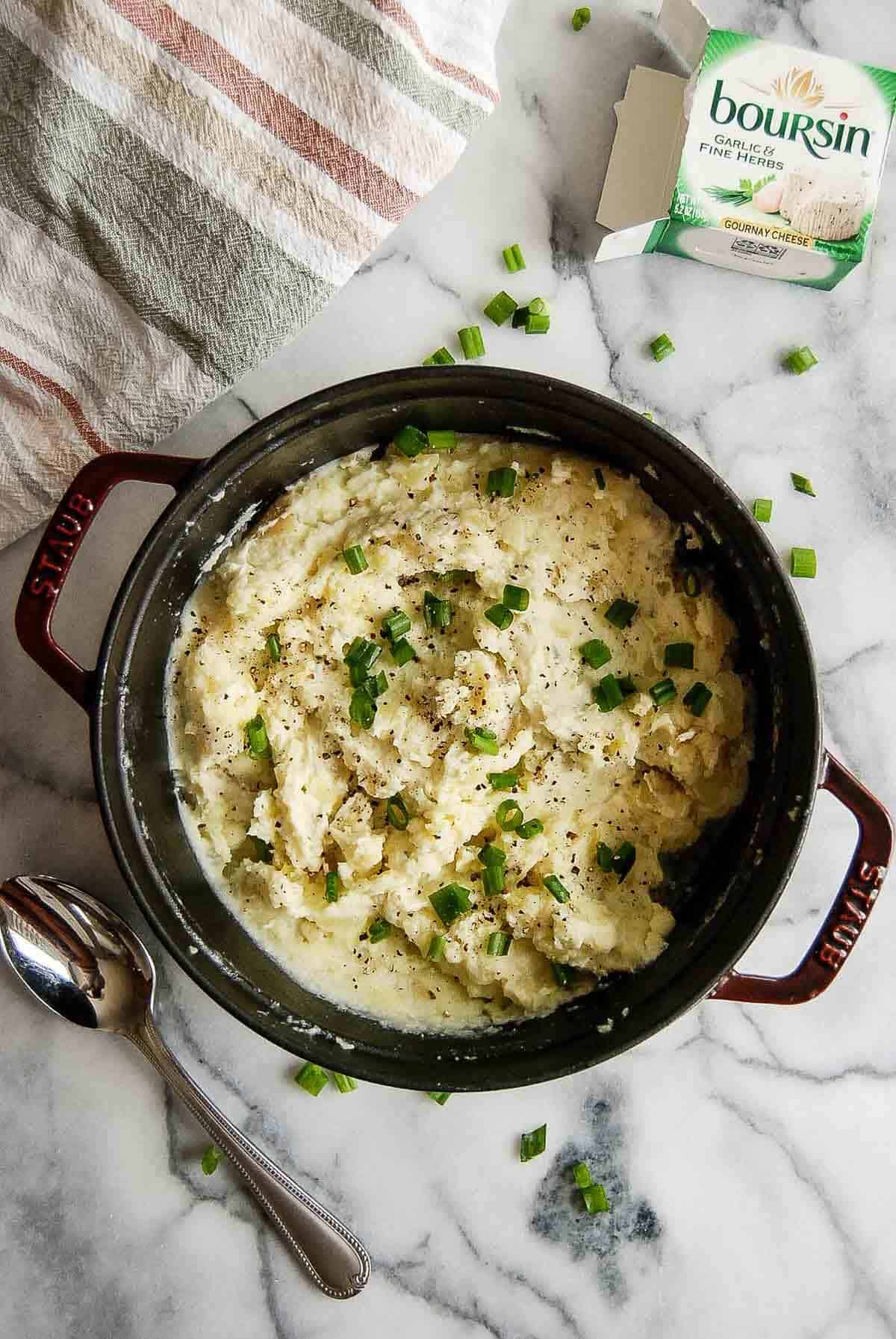 boursin mashed potatoes in pot on countertop, with chopped green onions sprinkled on top.