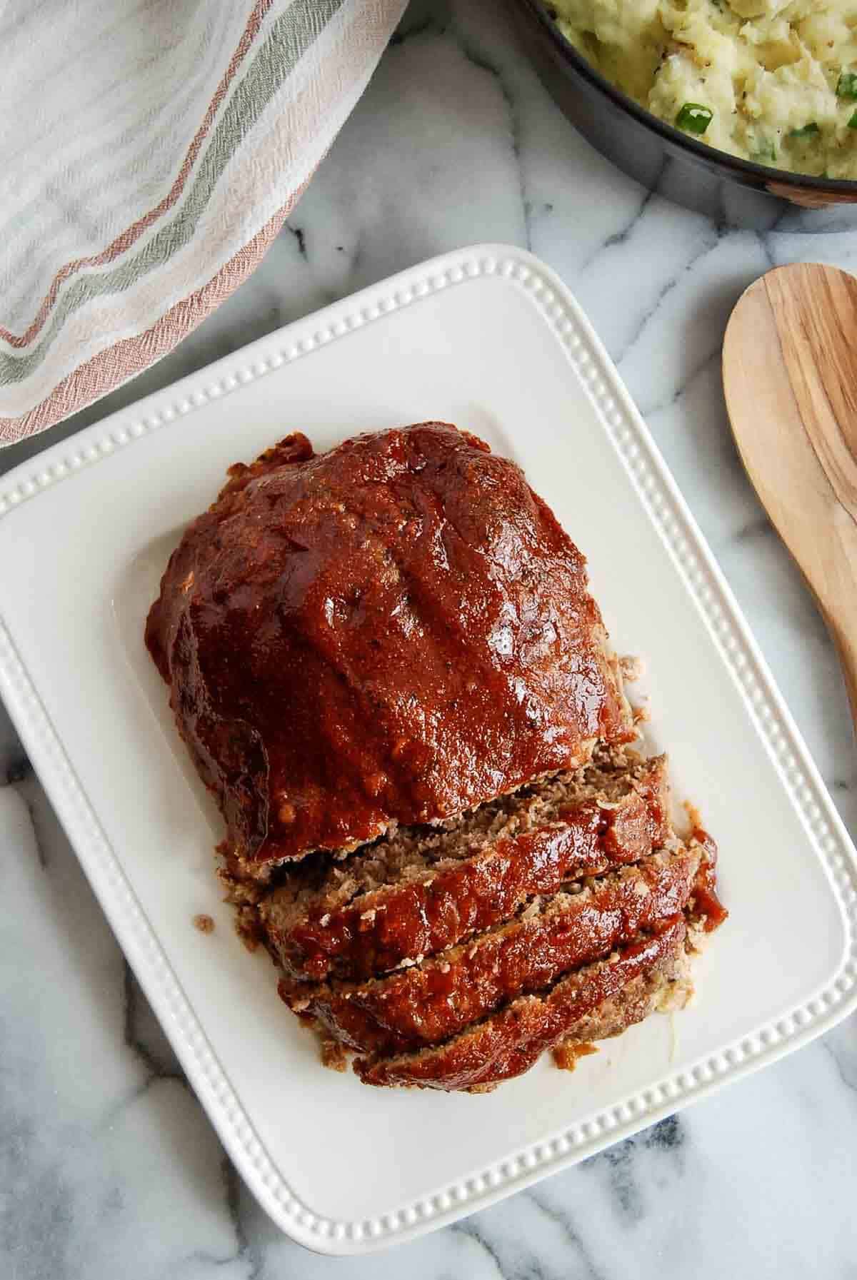 sliced lipton onion soup meatloaf on serving platter with mashed potatoes on the side.