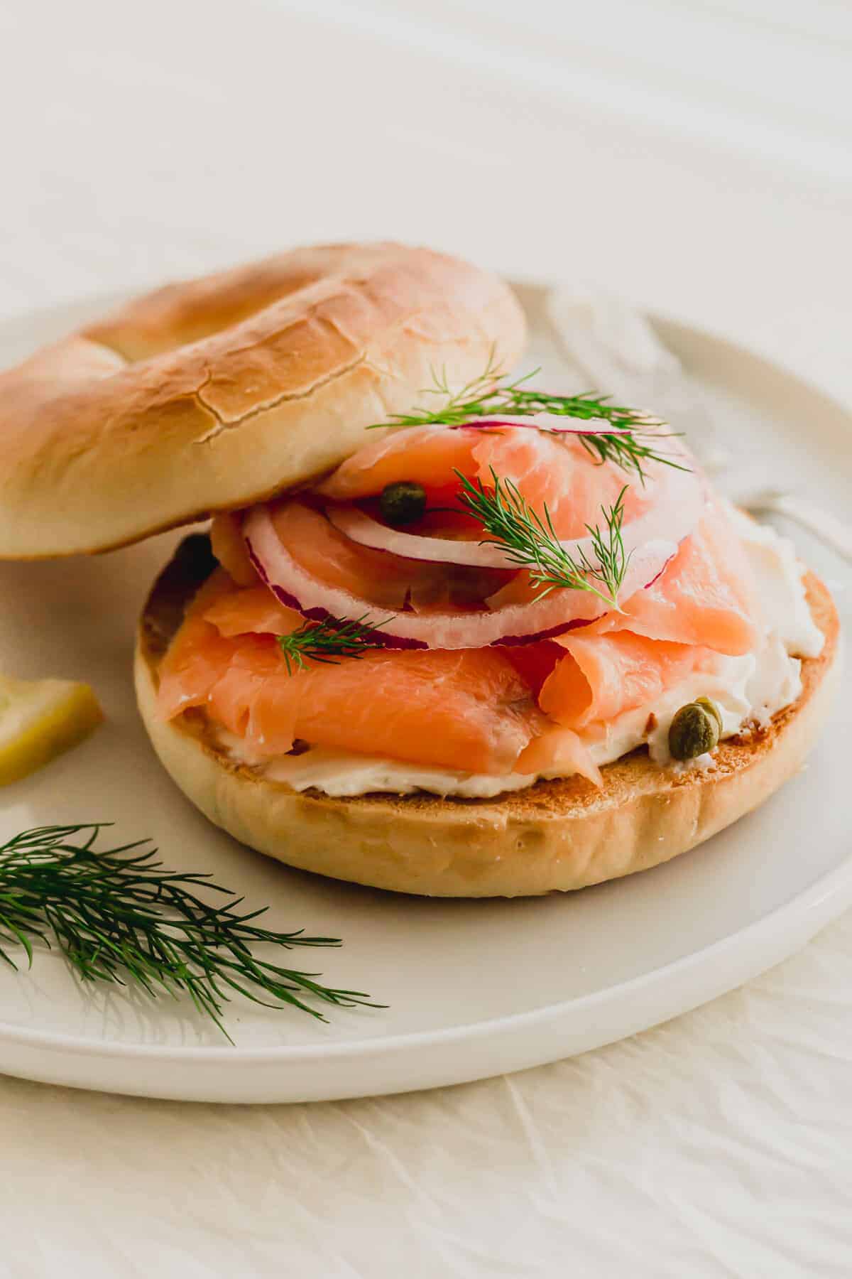 smoked salmon bagel sandwich with dill and capers on plate.