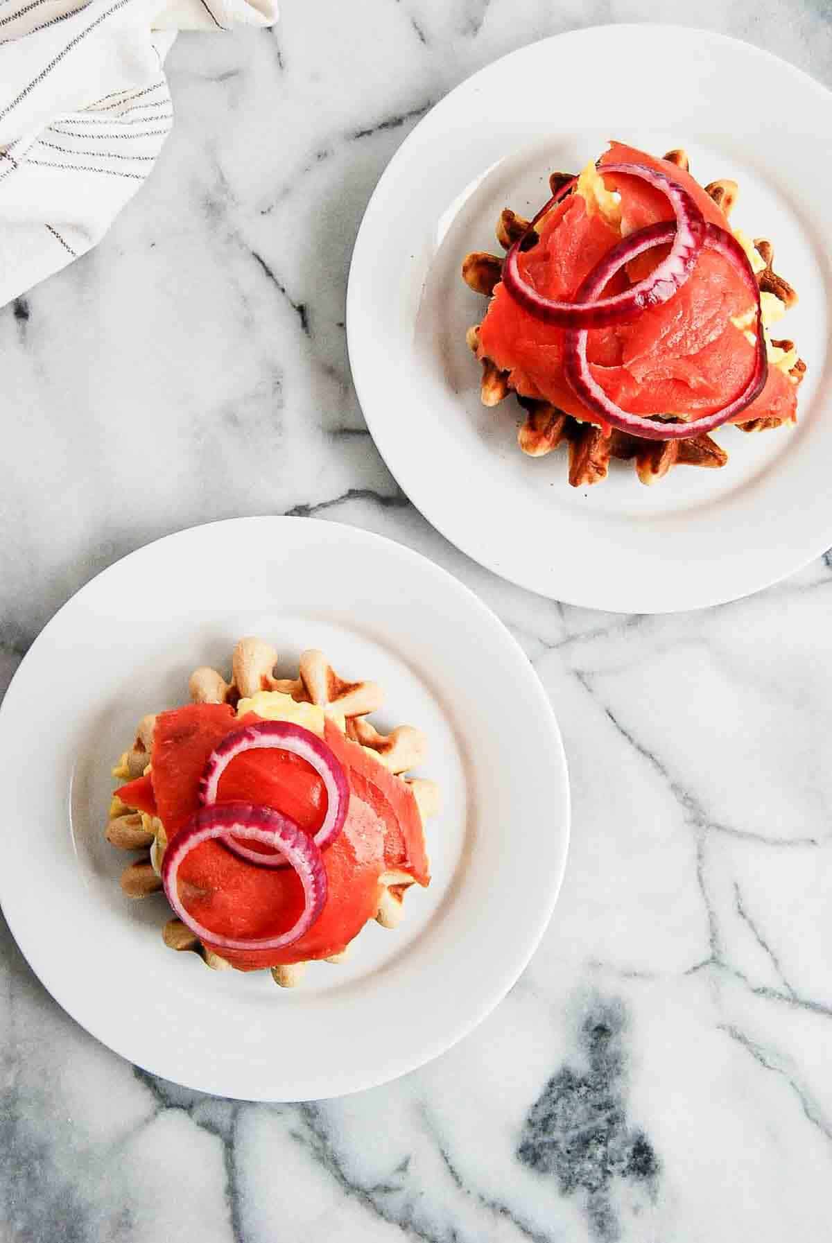 open faced waffle breakfast sandwiches on plates, sitting on countertop.