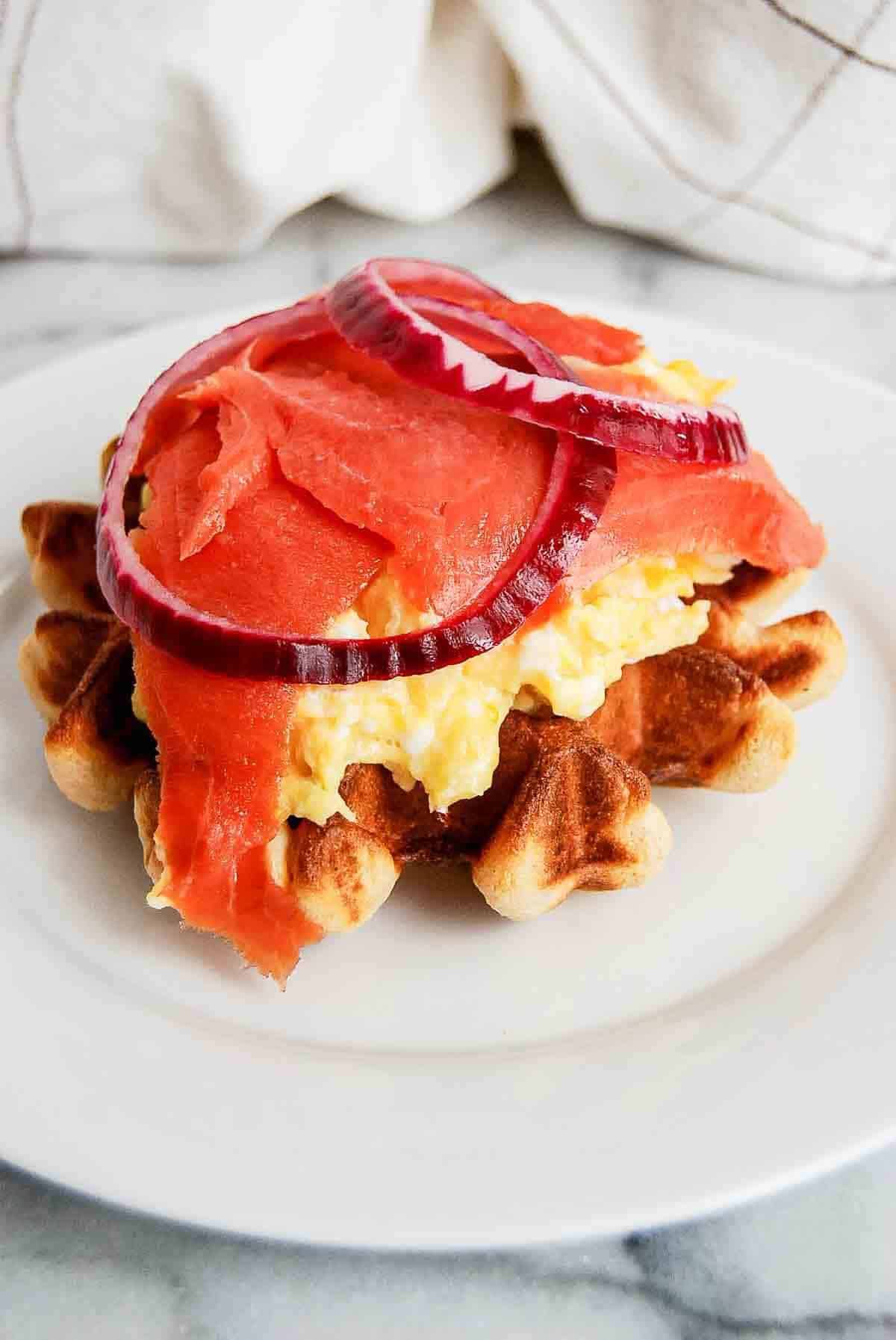 open faced waffle breakfast sandwich with smoked salmon, egg and cream cheese on plate.