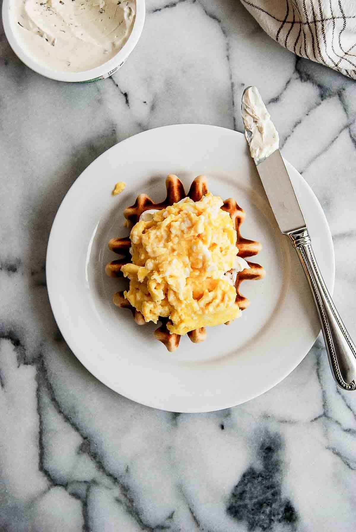 waffle with cream cheese and scrambled eggs on plate.