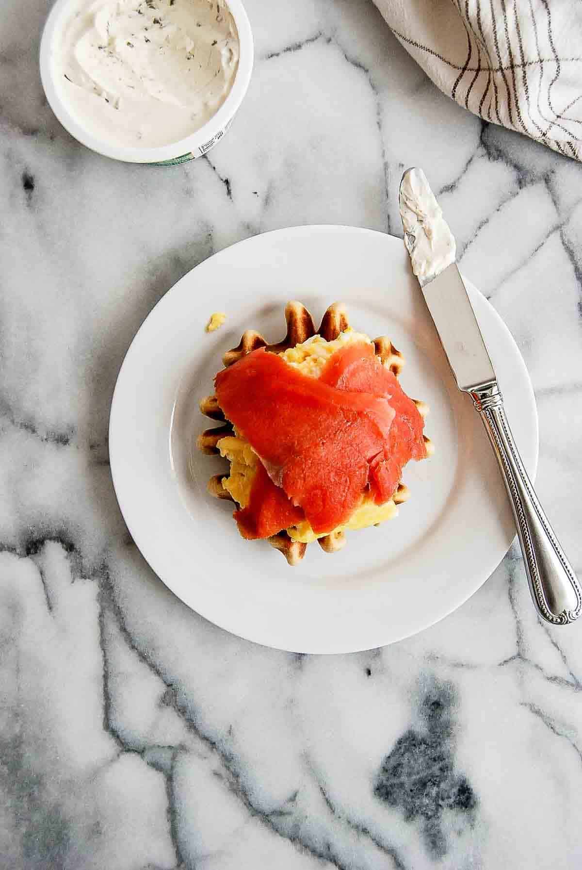 waffle breakfast sandwich with cream cheese, scrambled eggs and smoked salmon on plate.