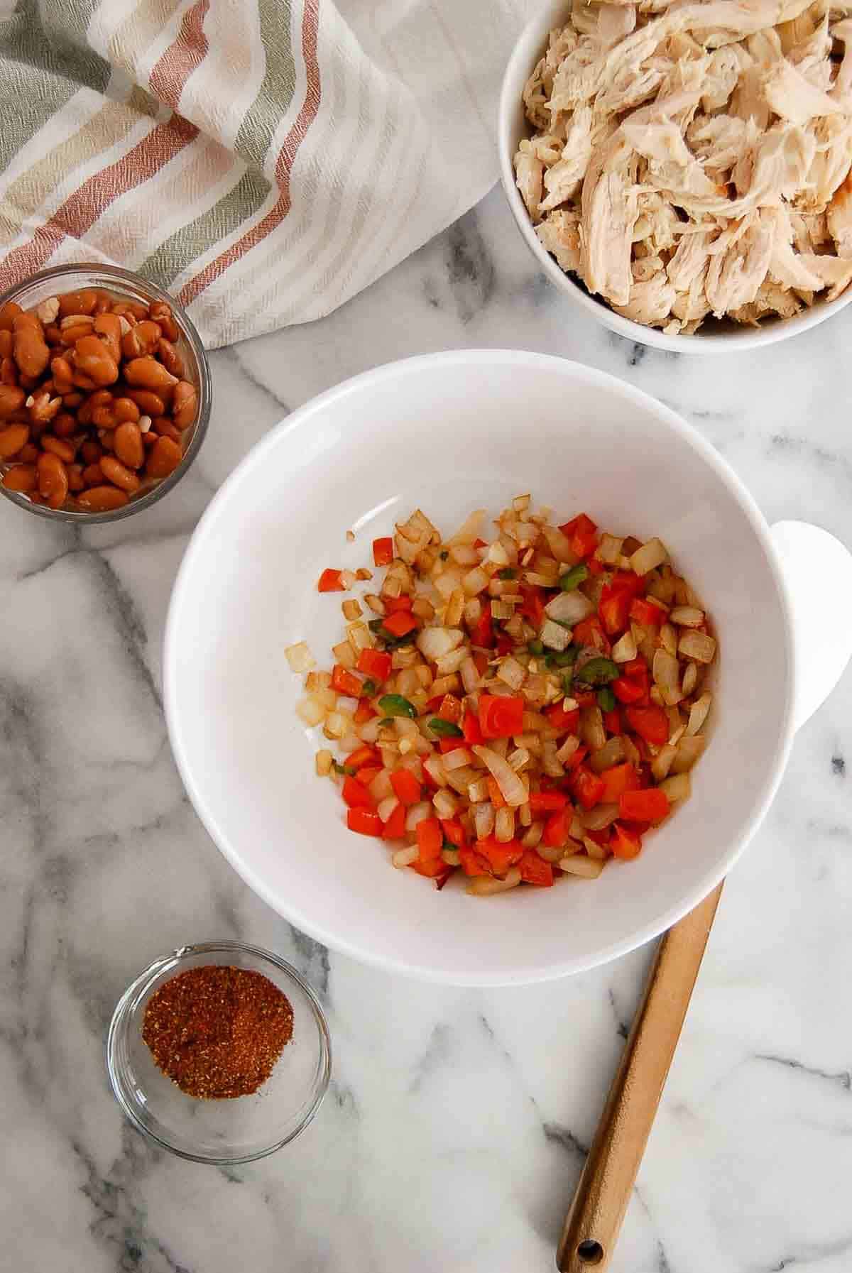 sautéed peppers and onions in bowl with chicken, beans and spices on the side.