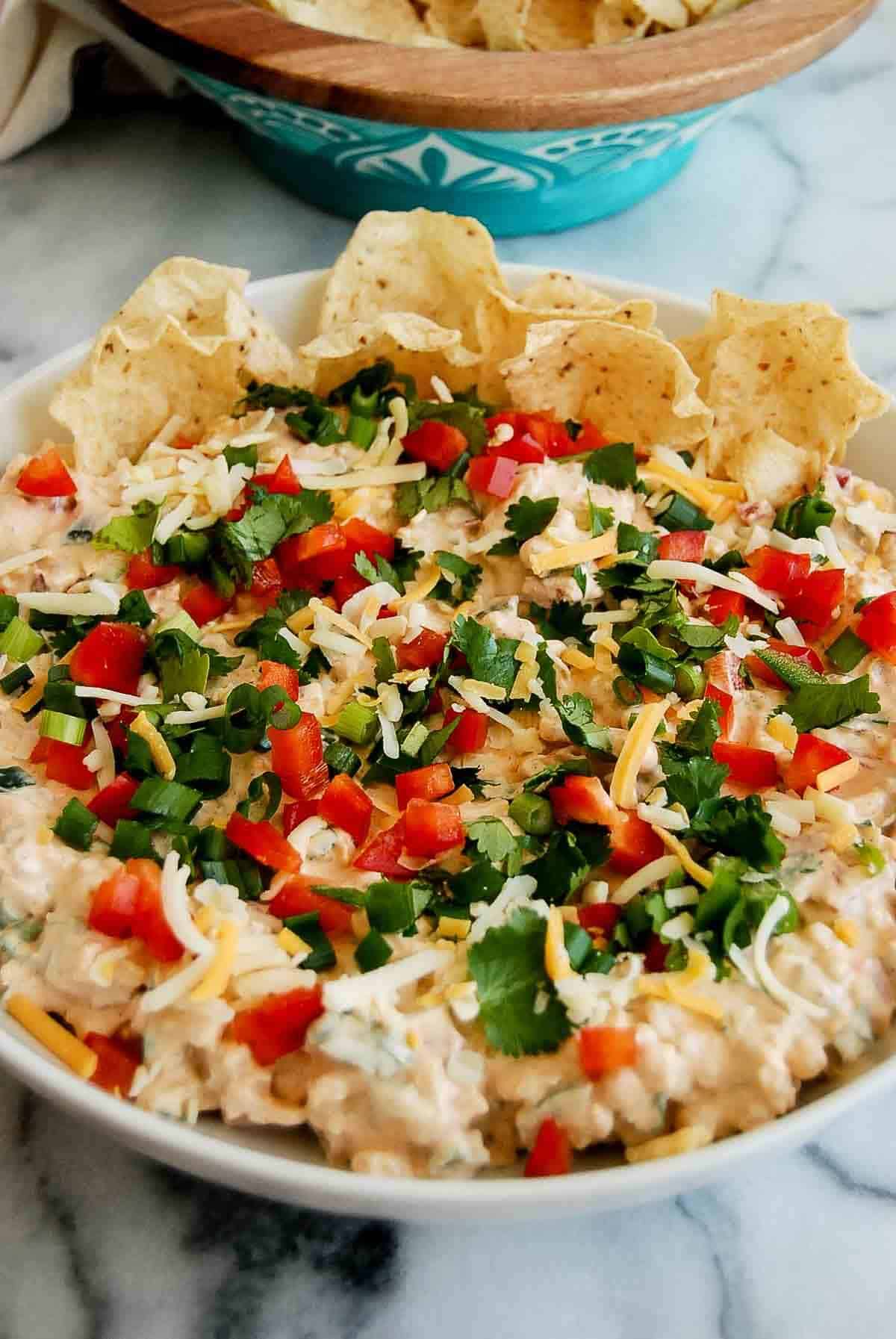 side view of corn dip with cream cheese in serving dish on countertop, with bowl of tortilla chips on the side.