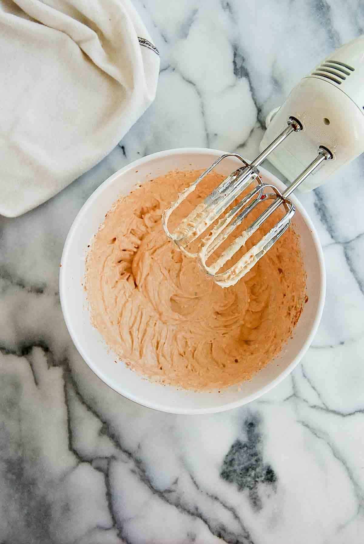 cream cheese and spices mixed in bowl with a hand mixer.