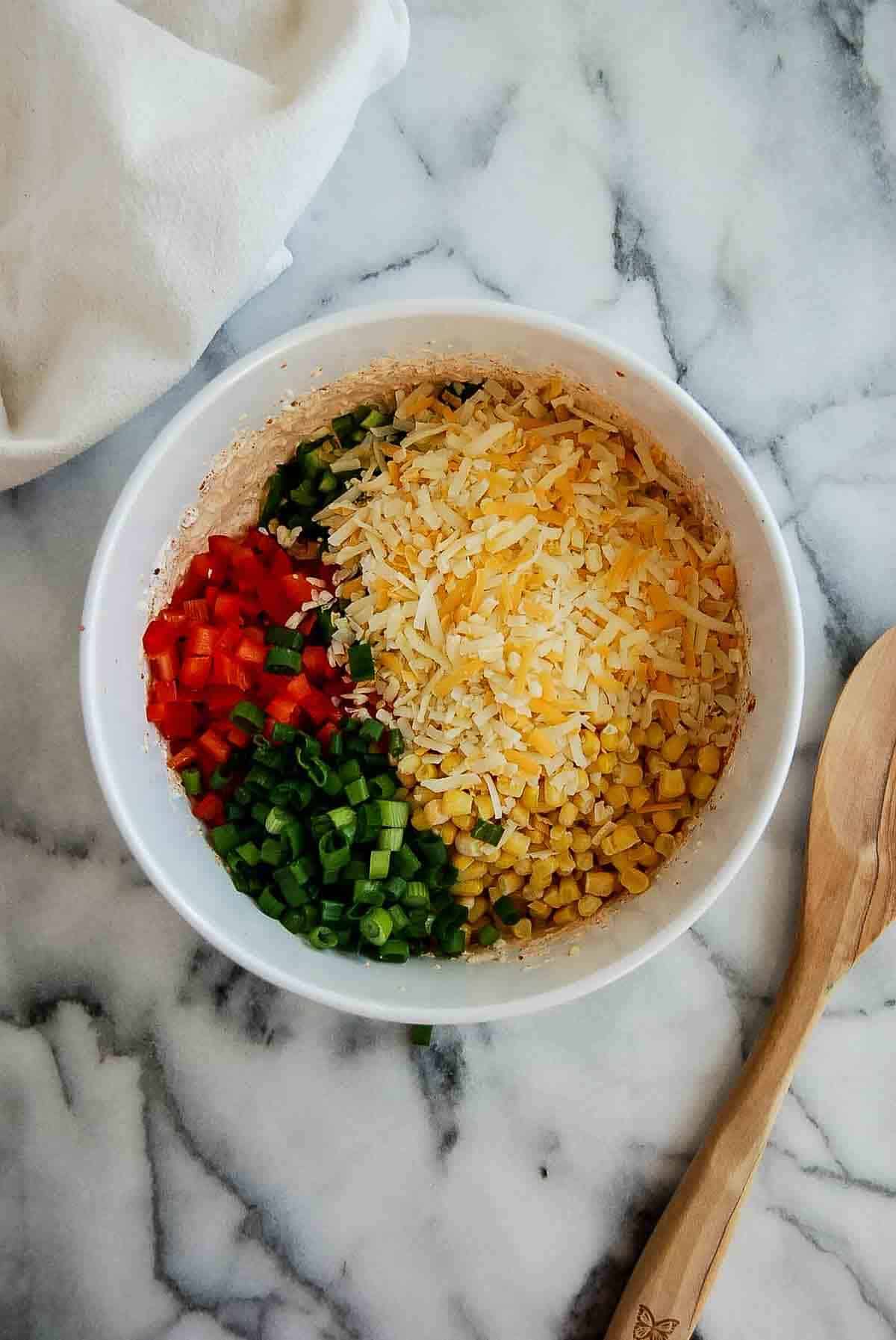 cream cheese, spices, corn, cheese and veggies all added to bowl on a countertop.