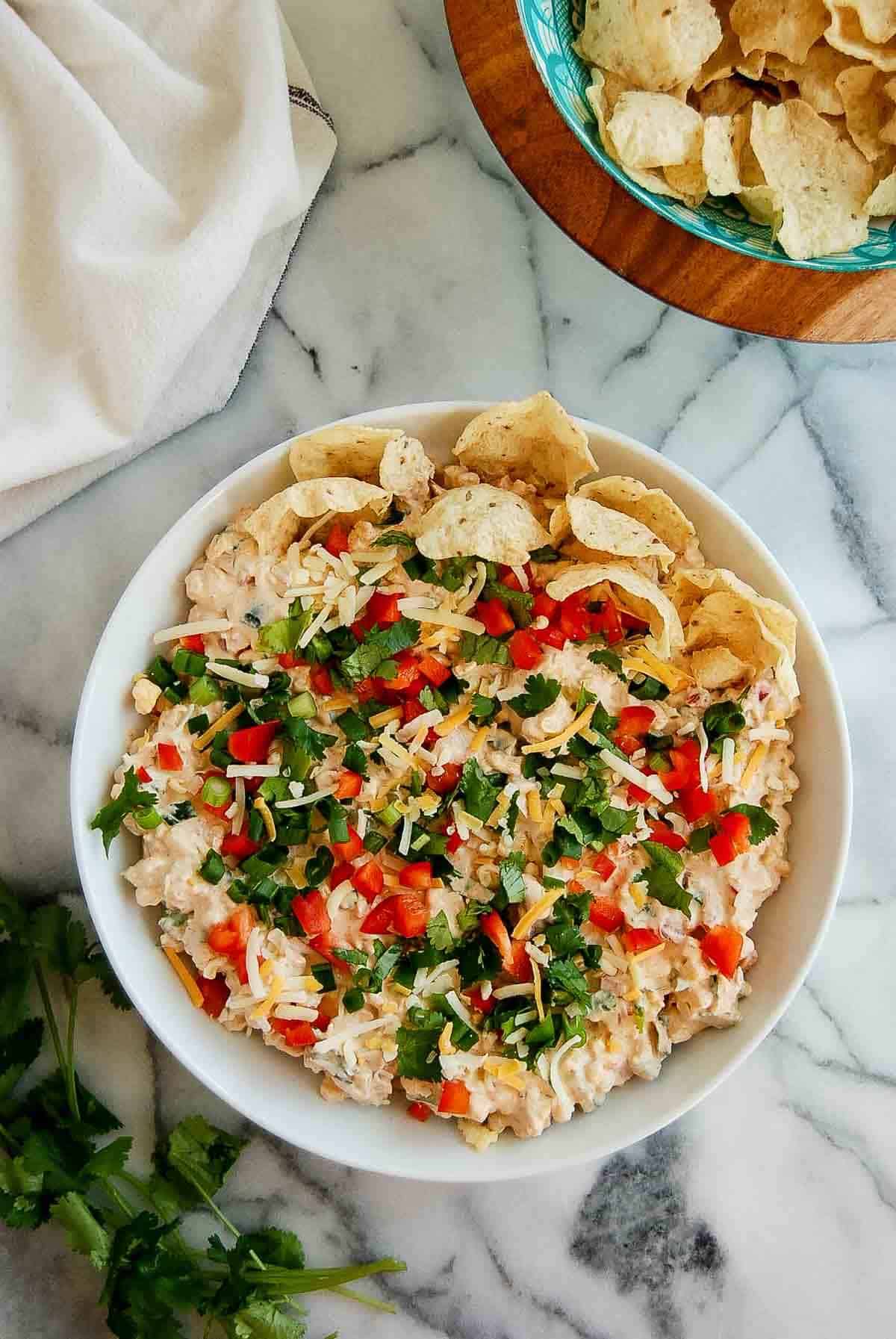 Corn dip with cream cheese in serving dish on countertop, with bowl of tortilla chips on the side.