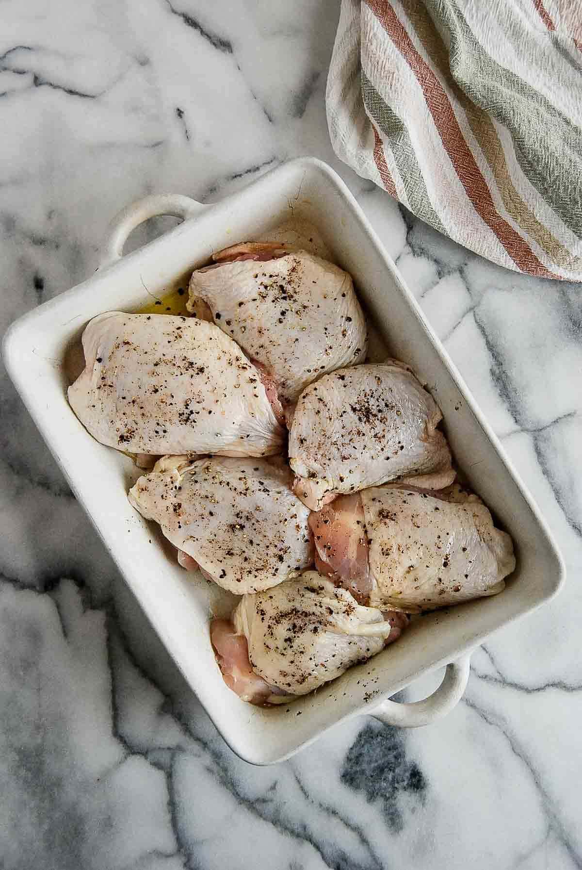 chicken things rubbed with oil and sprinkled with seasoning in baking dish.