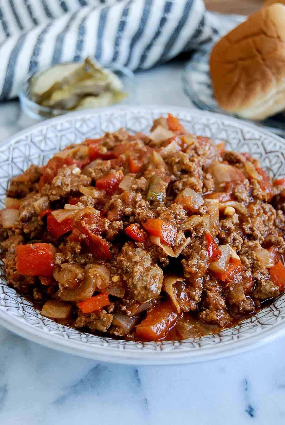 side view of sloppy joes with slider buns and pickles in the background.