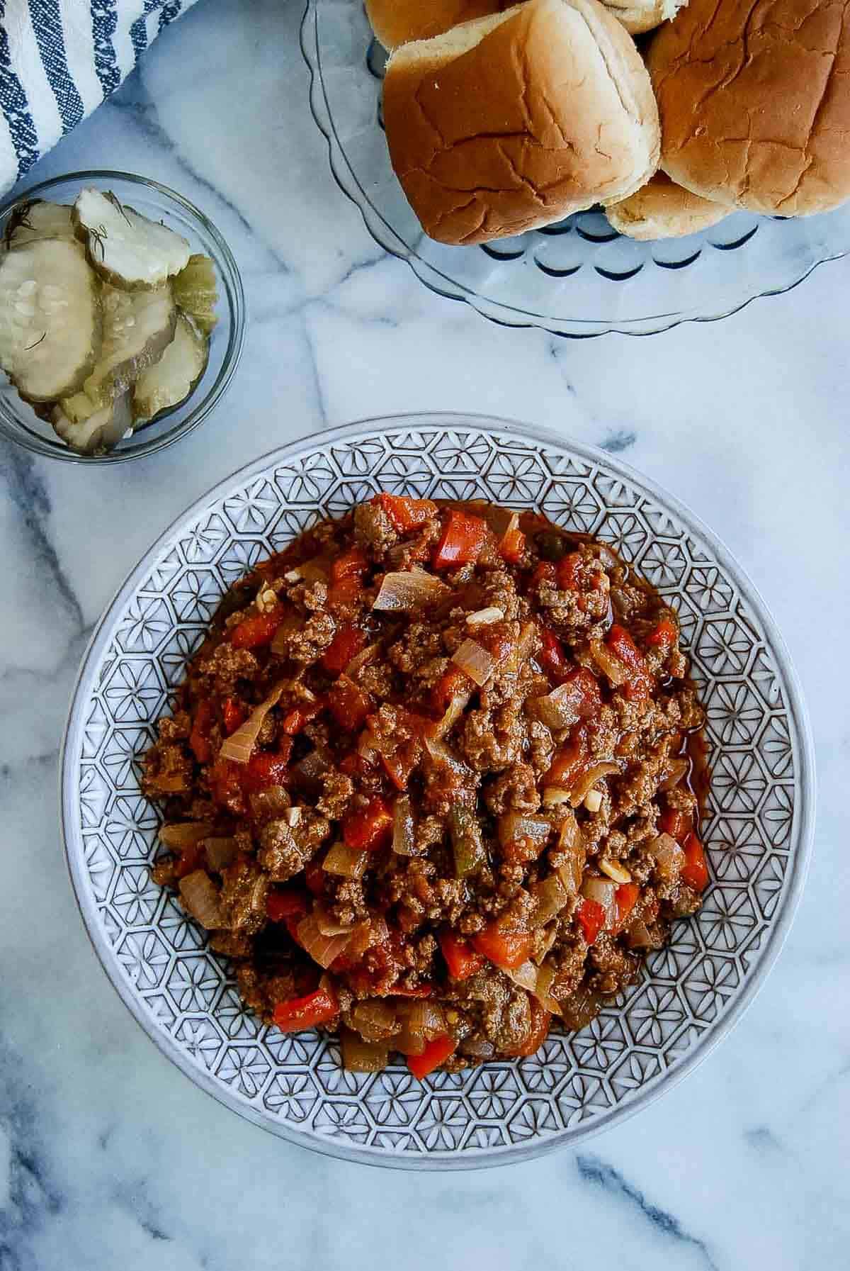 bowl of sloppy joes with slider buns and pickles to the side.