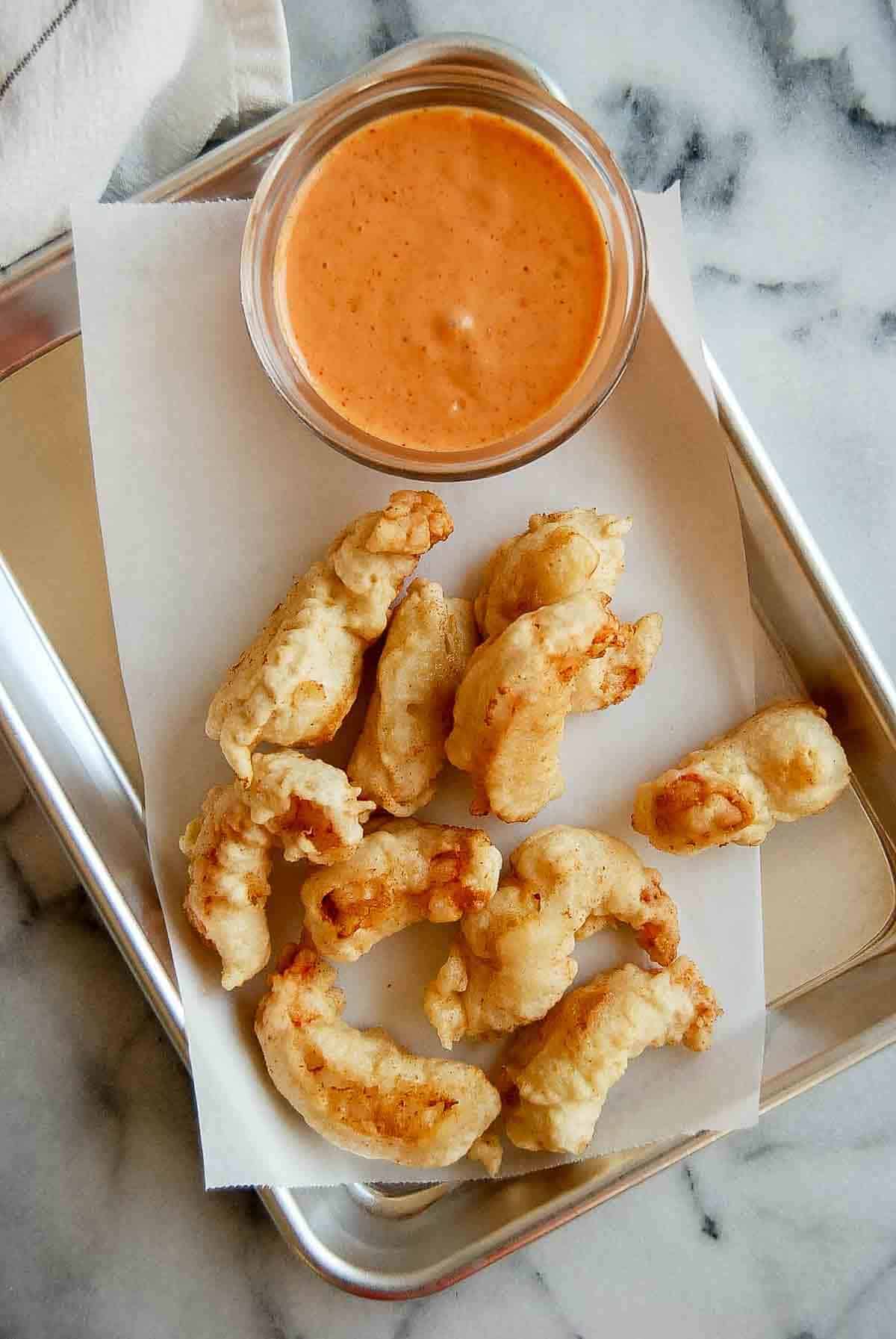 closeup of tempura shrimp on tray with dipping sauce on the side.