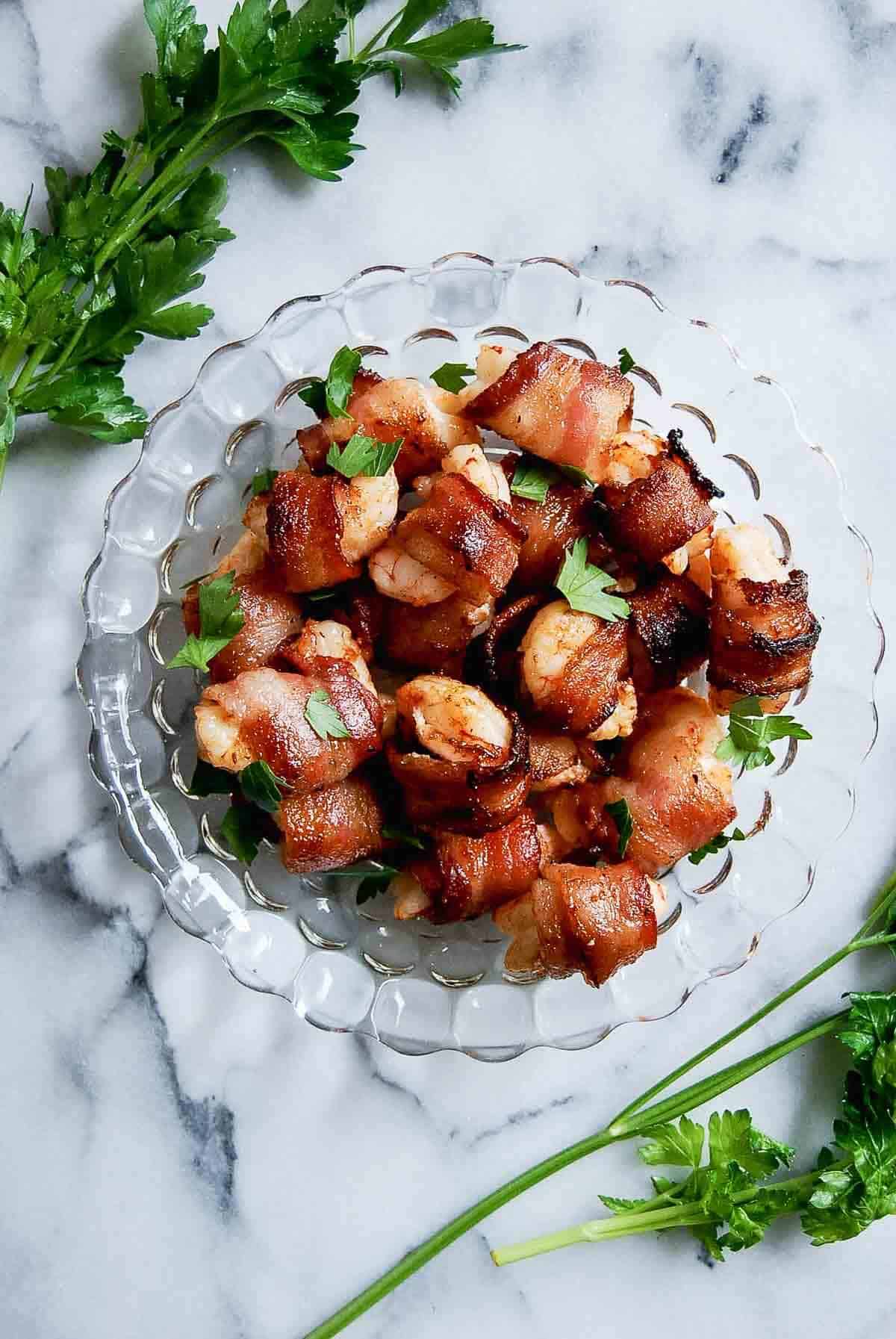 bacon wrapped shrimp on plate with parsley on the side.