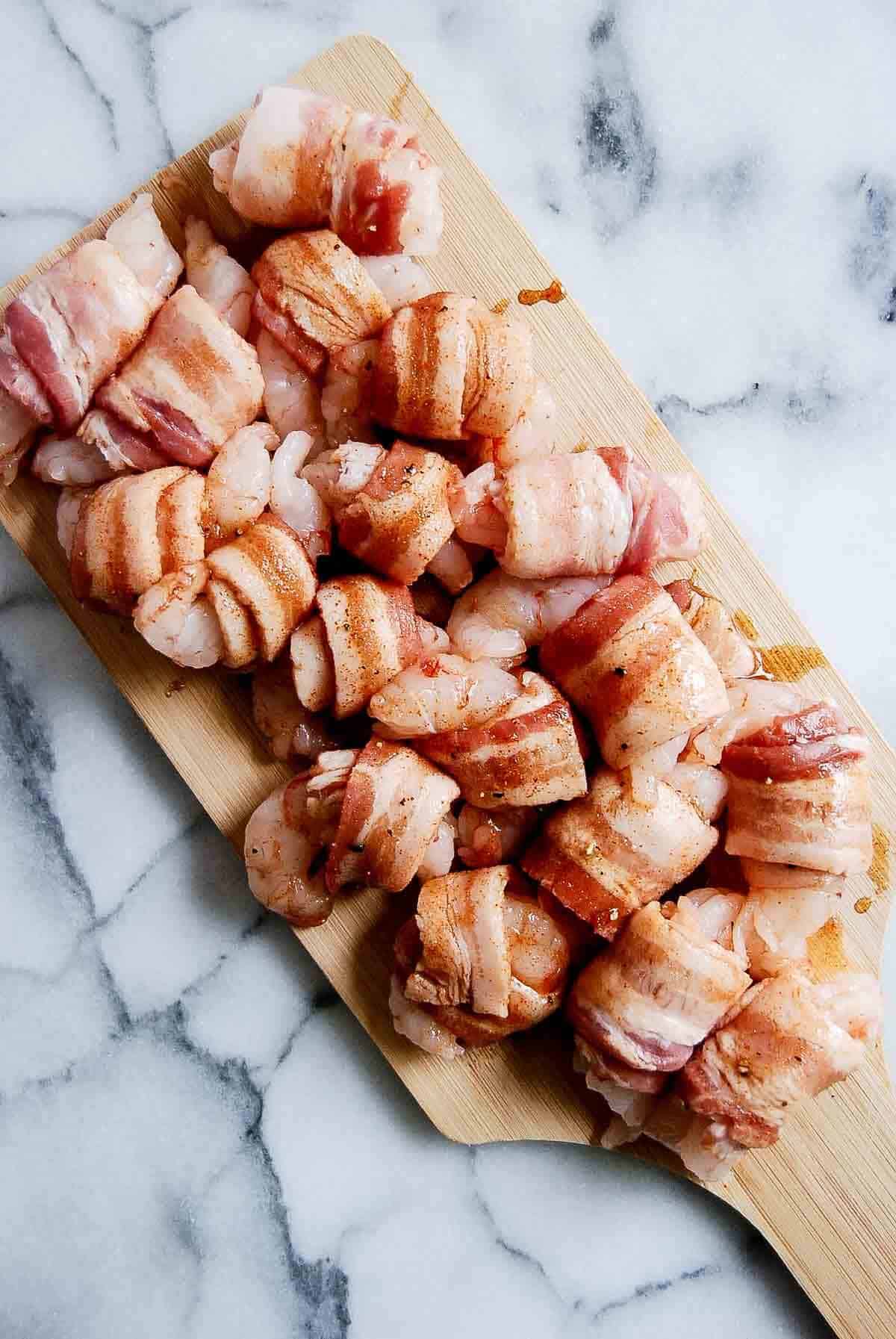 raw shrimp wrapped in bacon on cutting board.