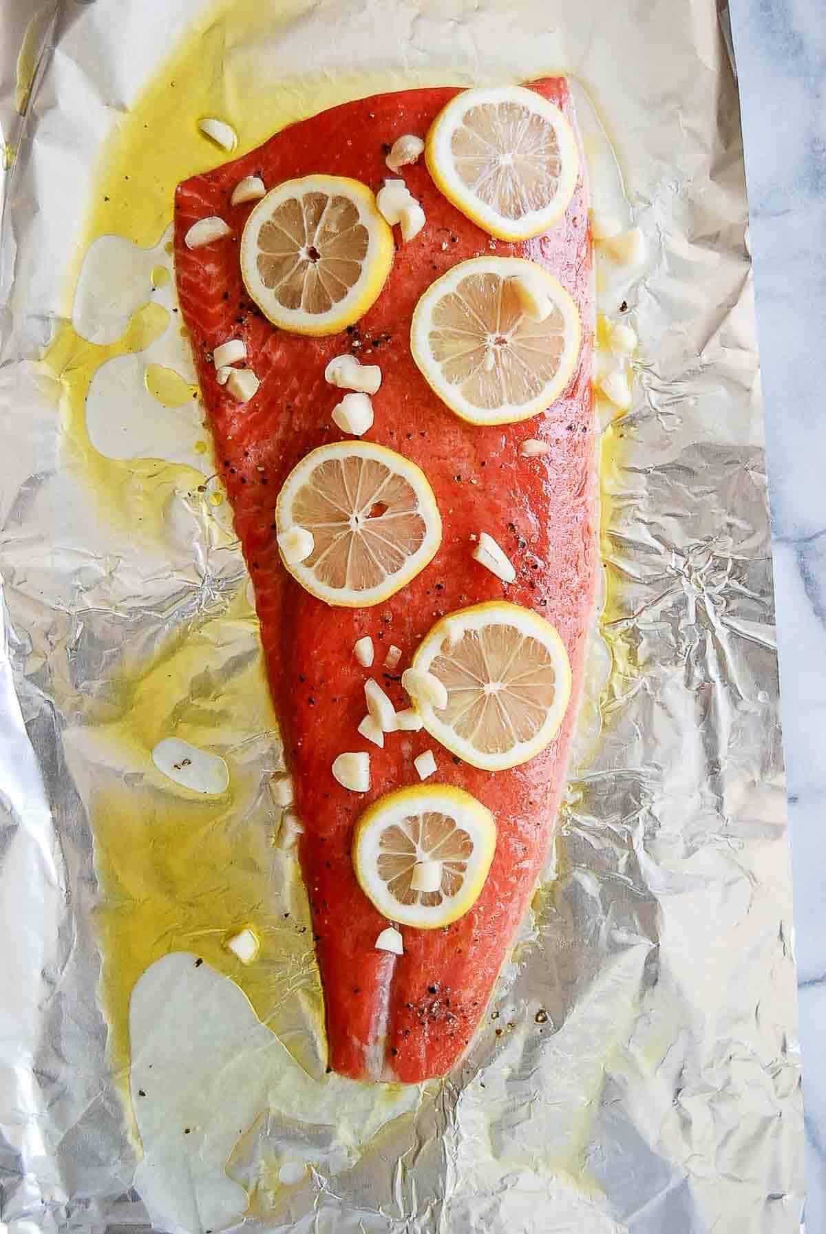 salmon on foil with lemon and garlic cloves sprinkled on top.