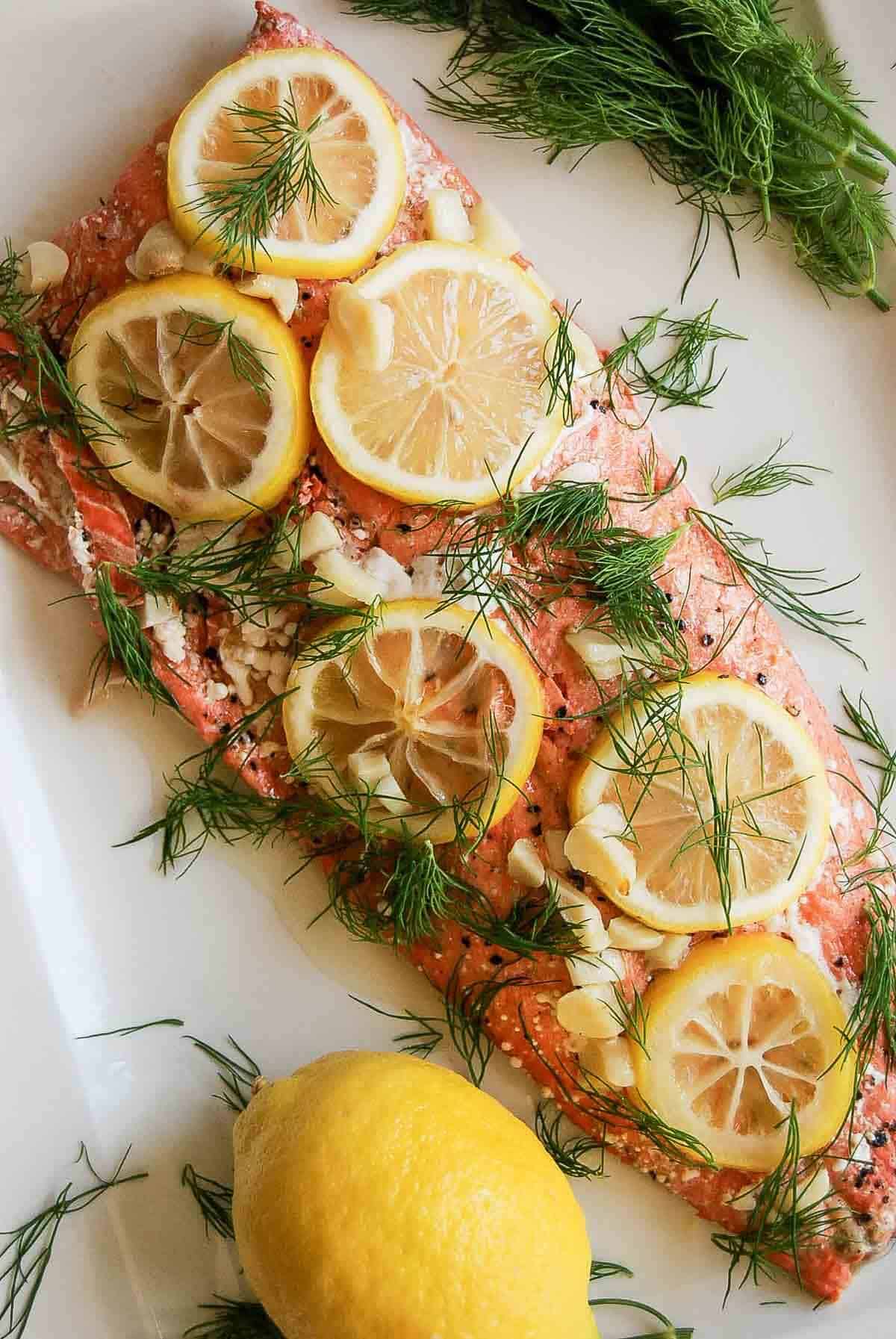 close up of baked salmon with lemon and dill on platter.
