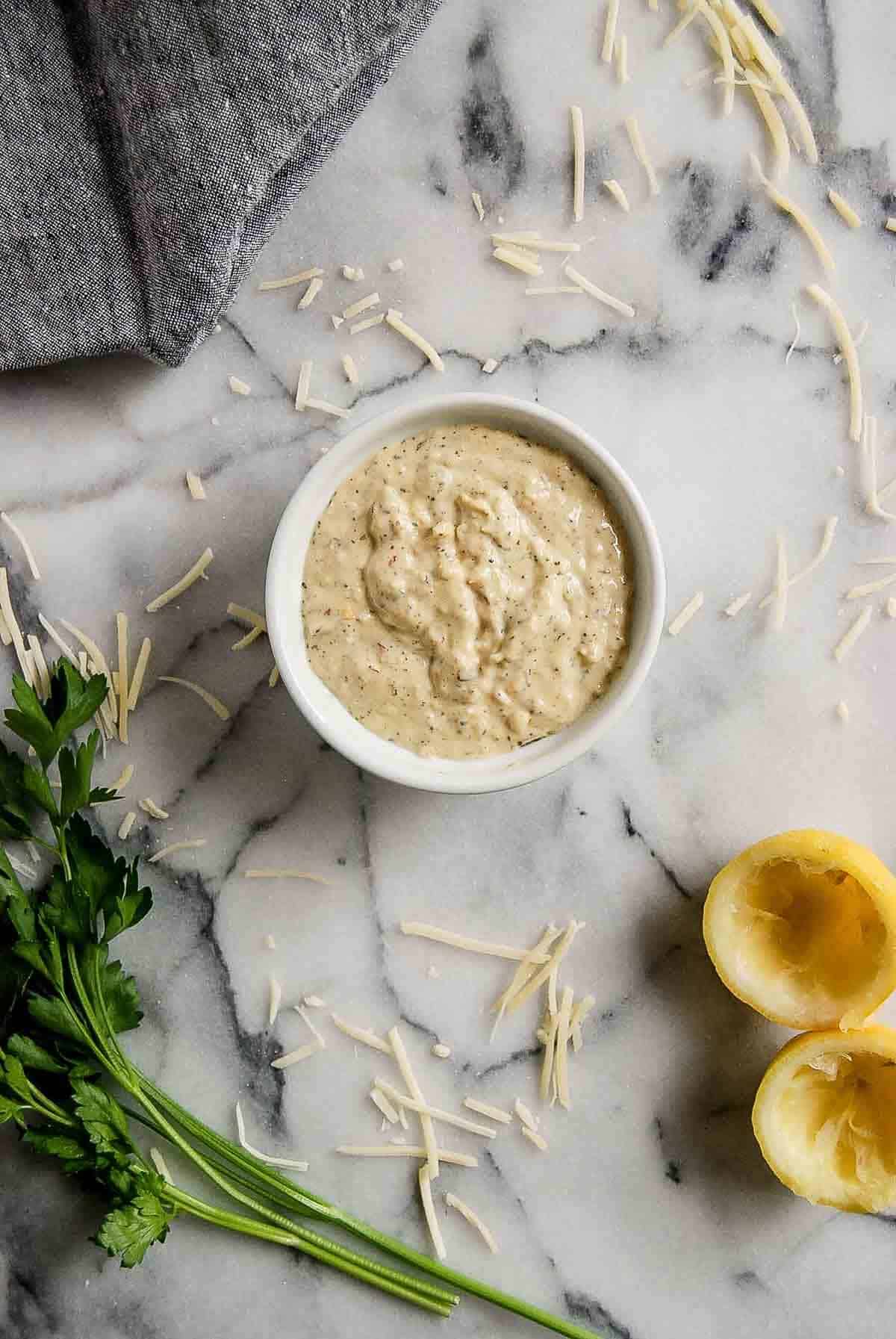 bowl of garlic parmesan sauce with lemon, parsley and parmesan sprinkled around.