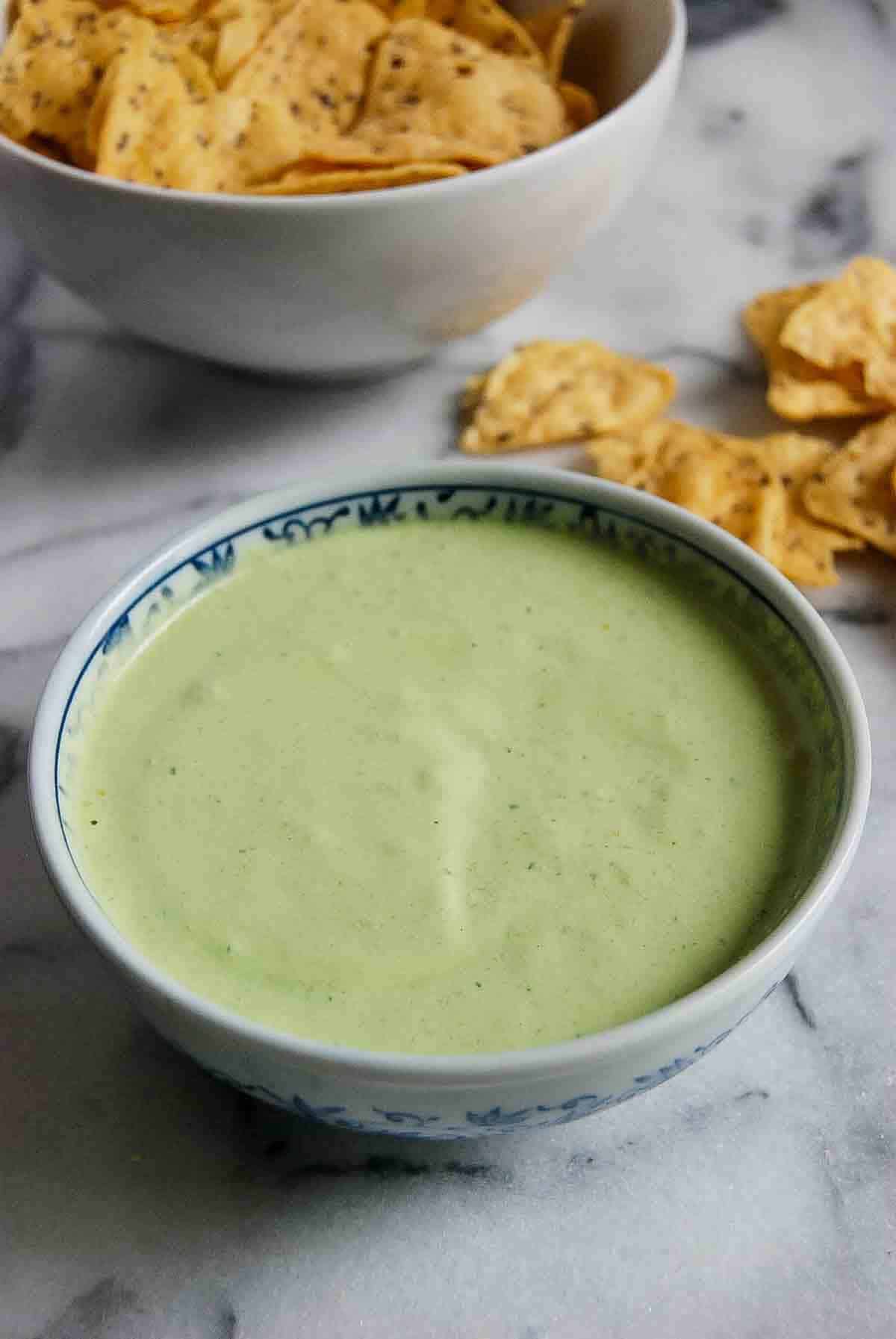 side view of bowl of green taco sauce with chips on countertop.