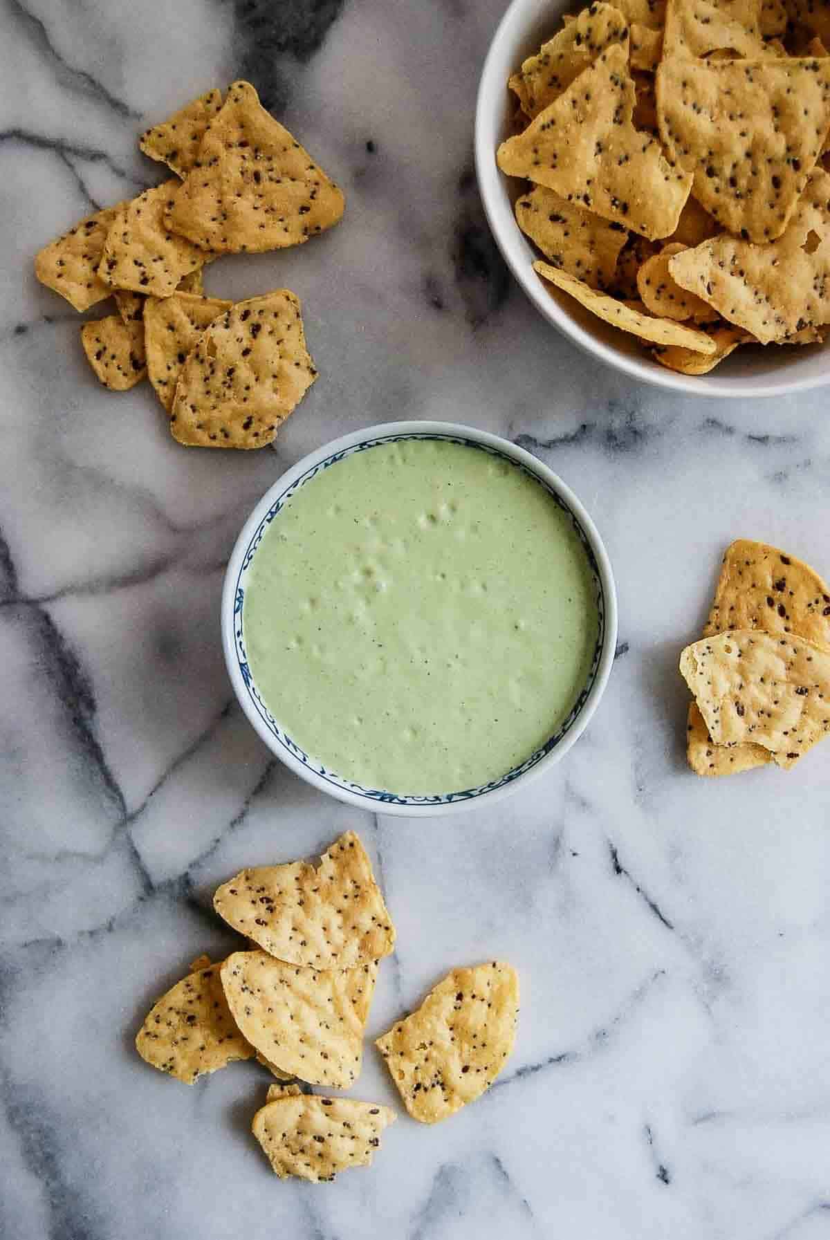 bowl of green taco sauce with chips on countertop.