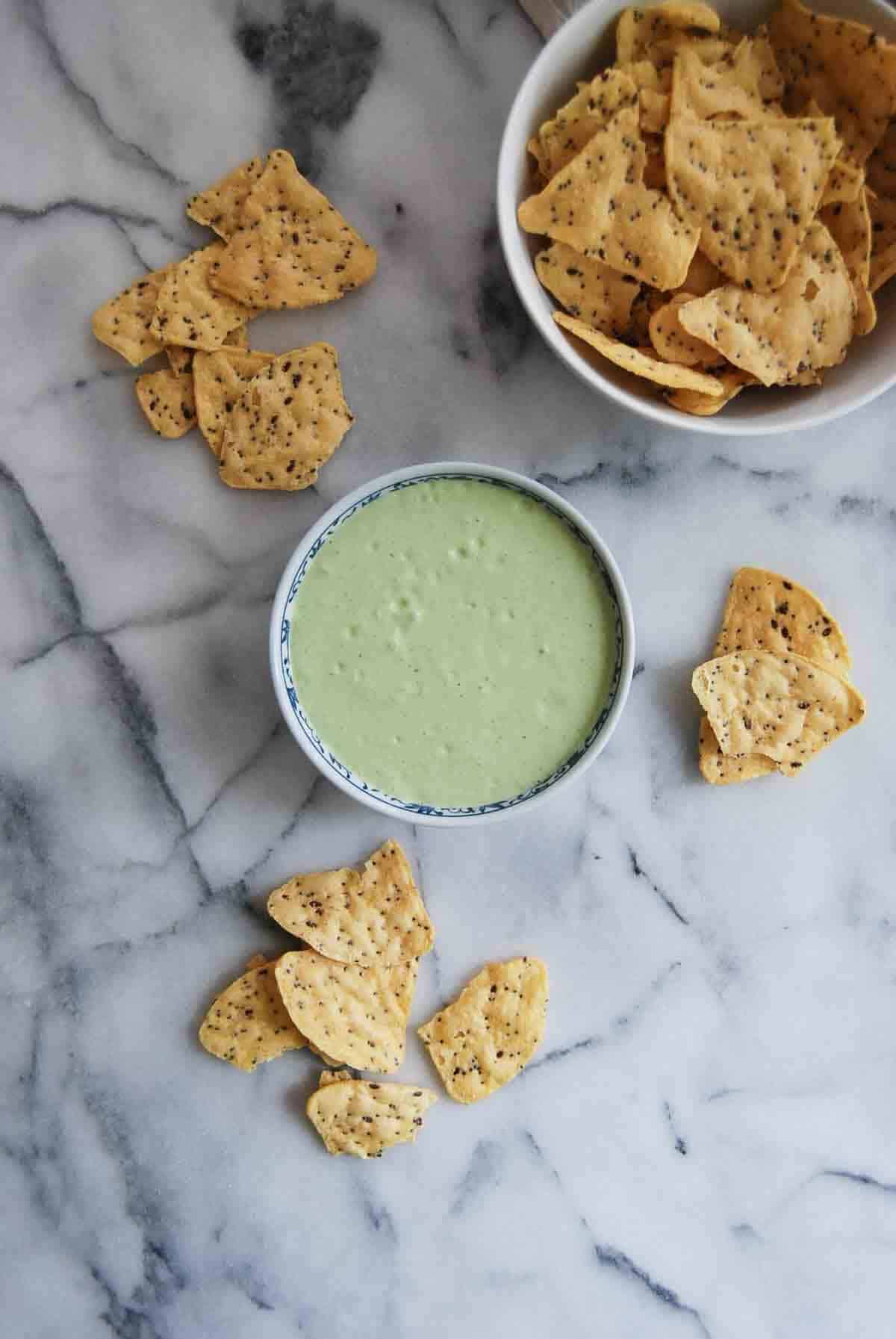 bowl of green taco sauce with chips on countertop.