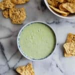 bowl of green taco sauce with chips on countertop.