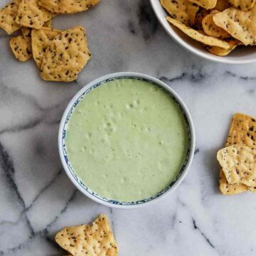 bowl of green taco sauce with chips on countertop.