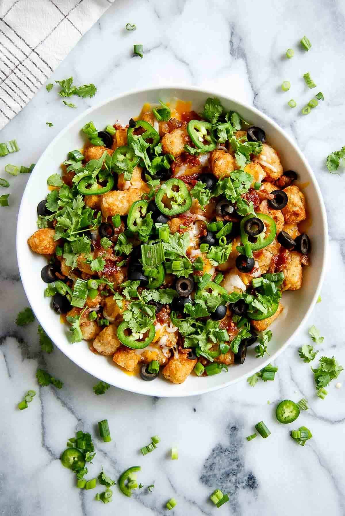 loaded tater tots with cheese, bacon, black olives, jalapeno and cilantro in bowl.
