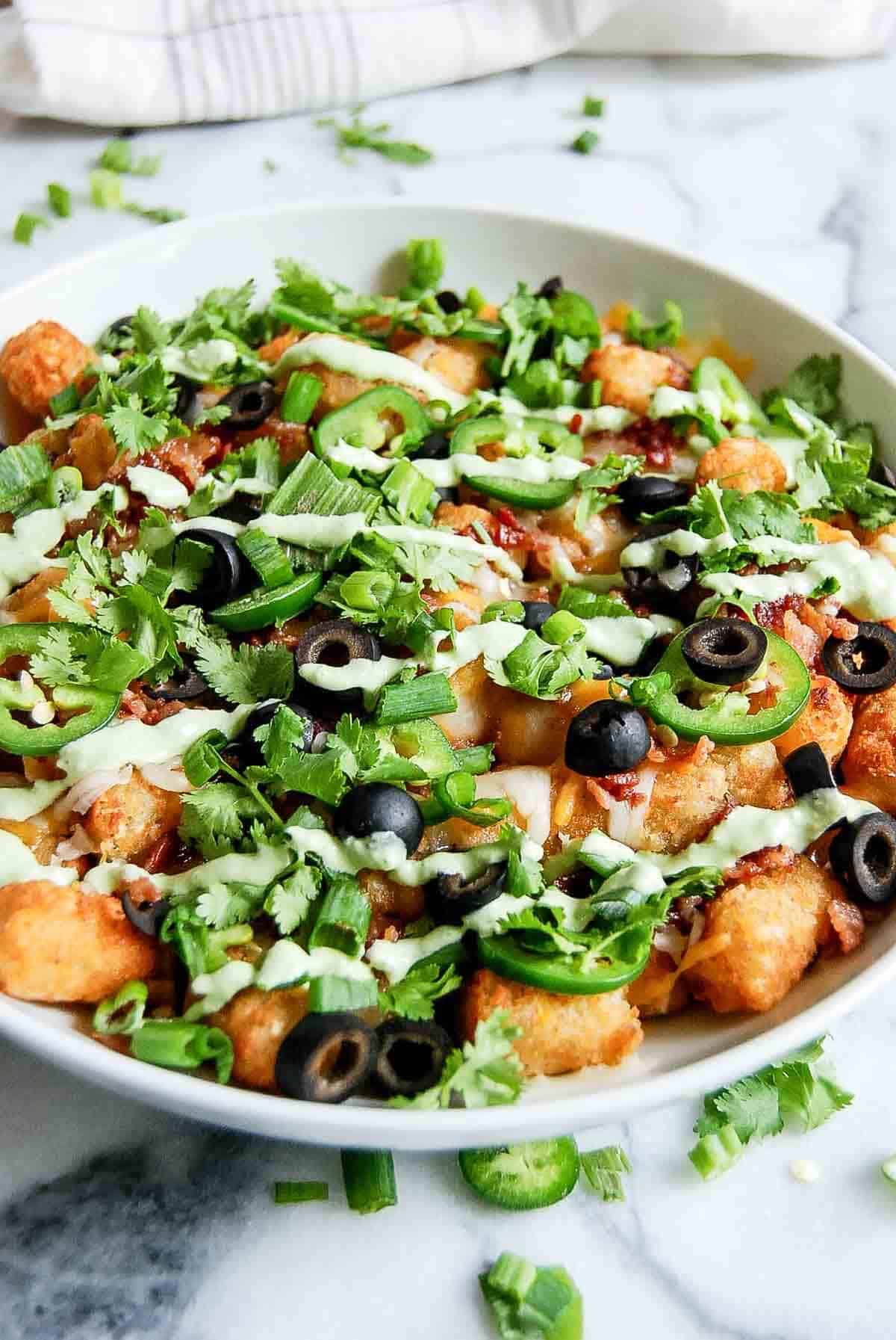 side view of loaded tater tots with cheese, bacon, black olives, jalapenos, cilantro and green sauce.