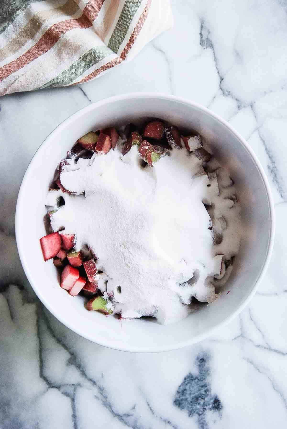 chopped rhubarb in bowl with sugar mixture on top.