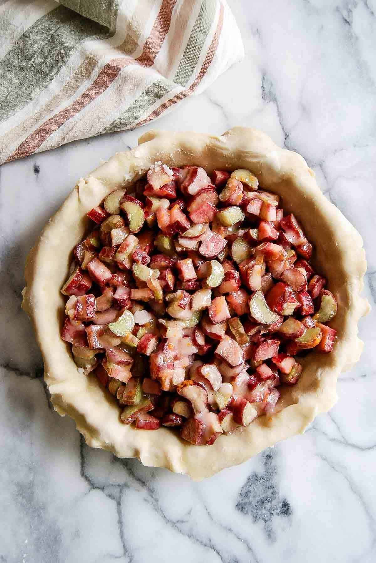 rolled out dough in pie plate with rhubarb filling mixture inside.