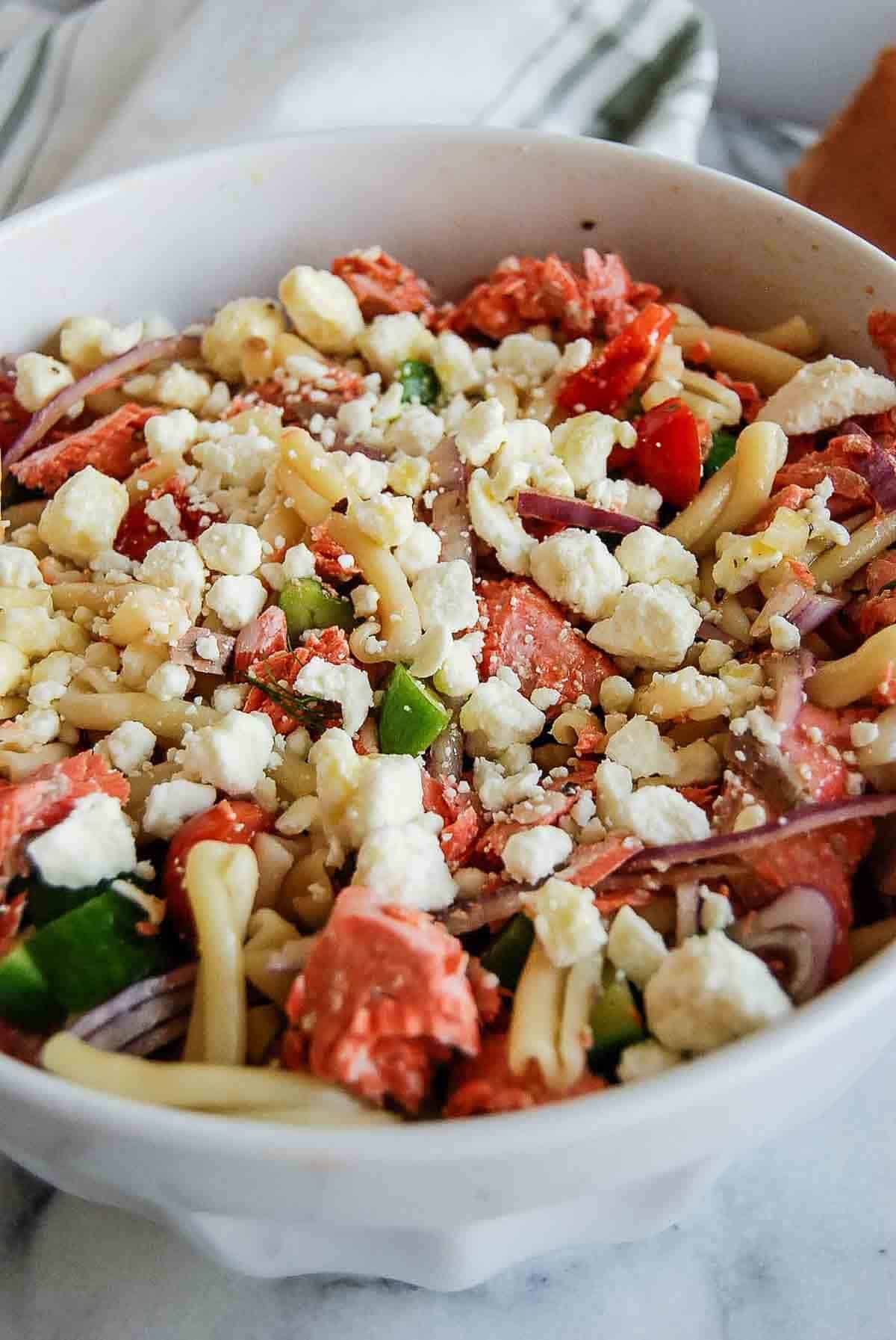 salmon pasta salad with veggies and feta in bowl on cutting board with baguette on the side.