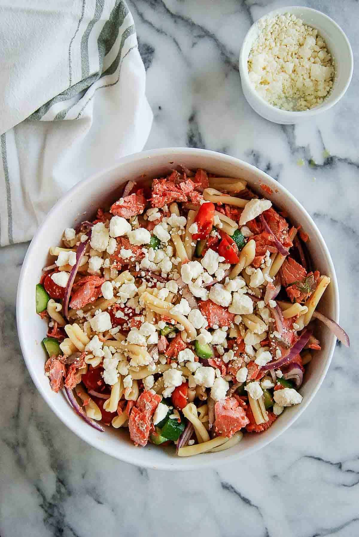salmon pasta salad with feta and veggies in bowl on countertop. with feta.