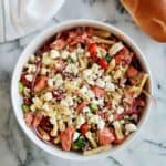 salmon pasta salad with veggies and feta in bowl on cutting board with baguette on the side.