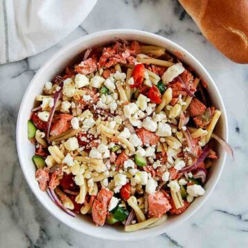 salmon pasta salad with veggies and feta in bowl on cutting board with baguette on the side.