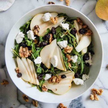 arugula pear and goat cheese salad in bowl on countertop.