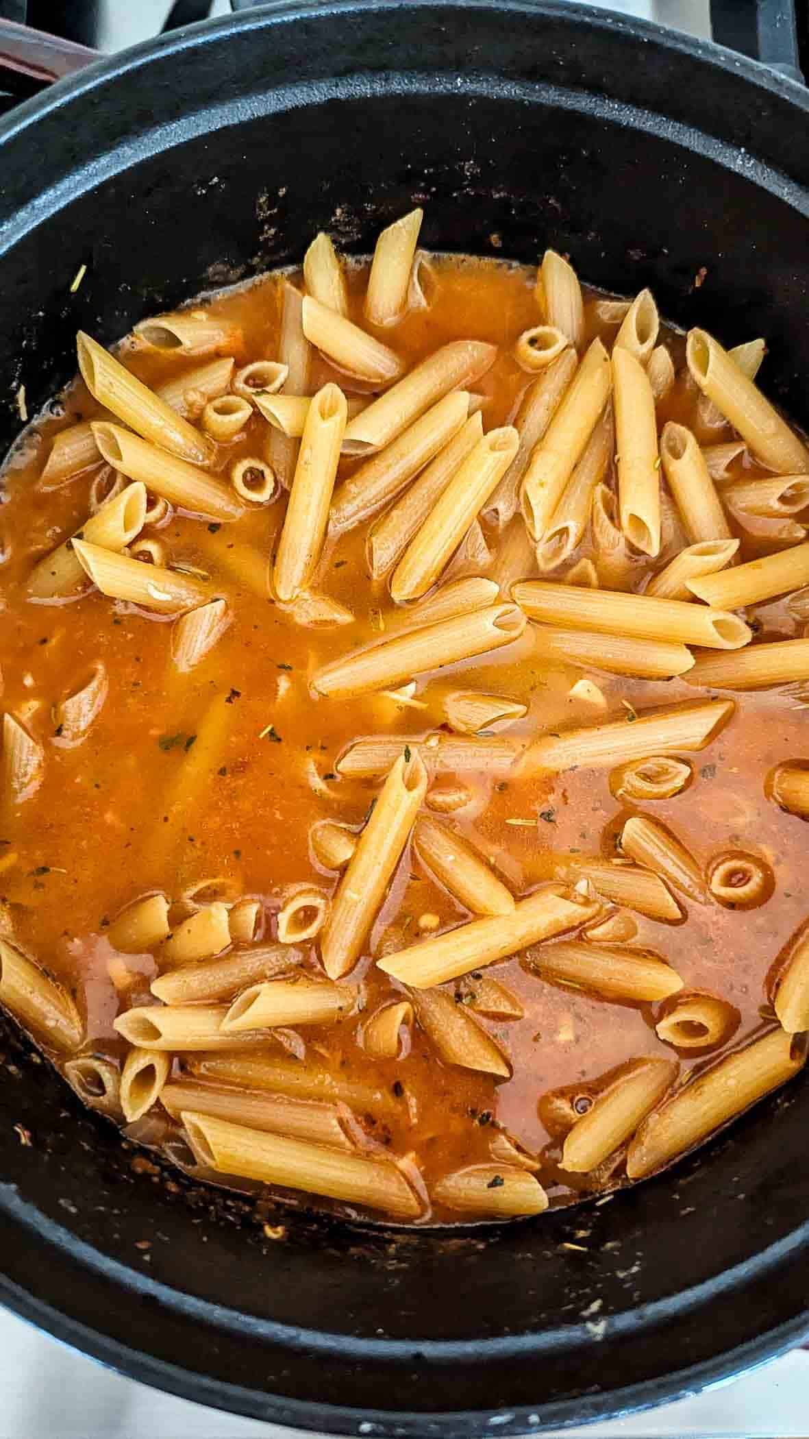 penne noodles cooking in chicken broth in pot.