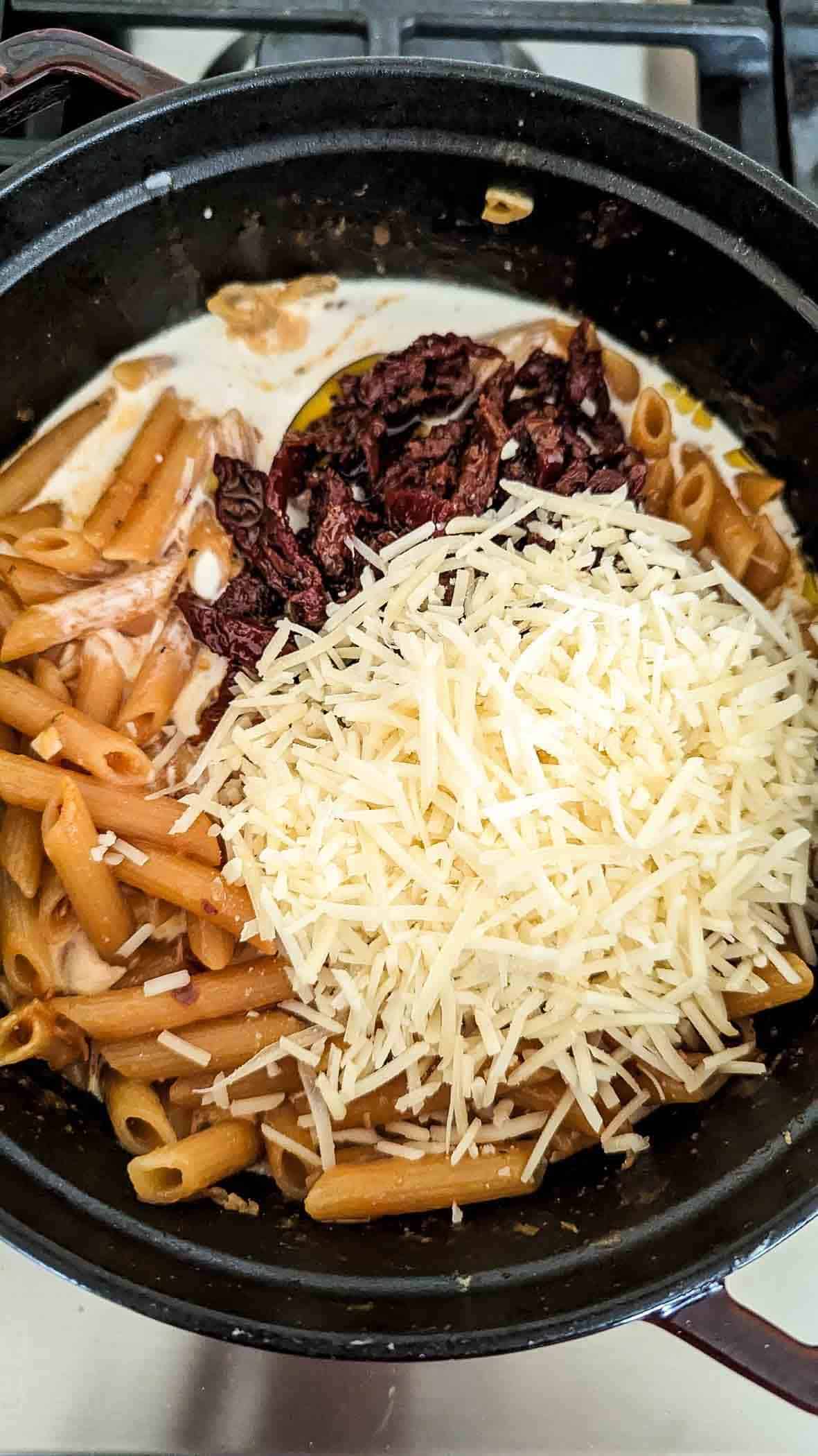 cooked pasta noodles in pot with cream, sun dried tomatoes and parmesan cheese.
