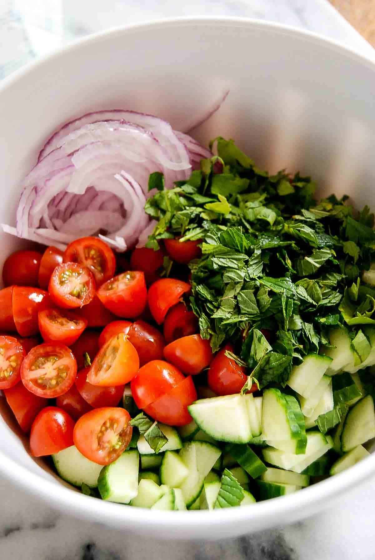 tomatoes, cucumbers, mint, parsley and red onion in bowl.