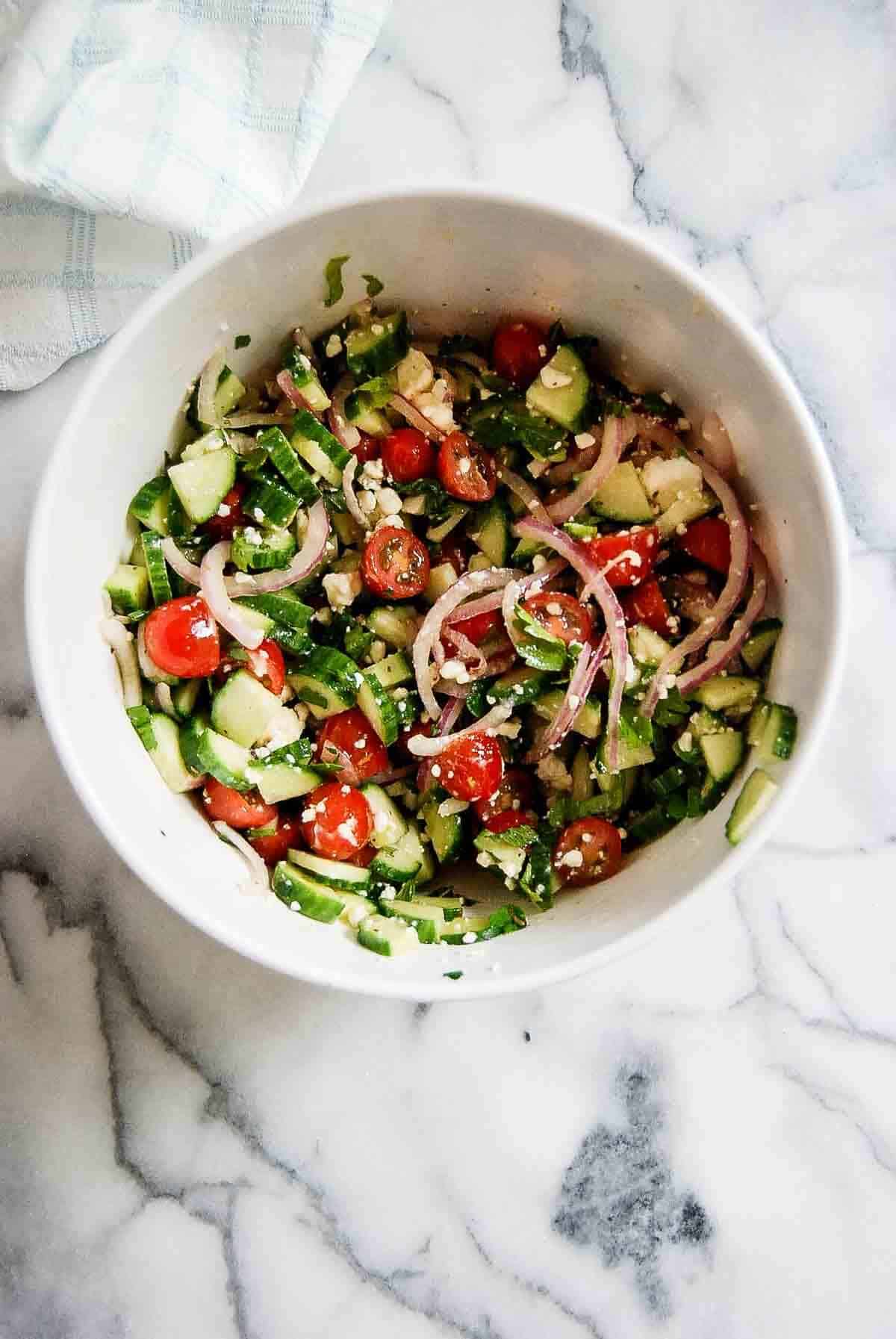 Mediterranean cucumber and tomato salad in bowl on countertop.