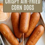 A tray with five crispy air fryer corn dogs on sticks, paired with a bowl of dipping sauce. Text overlay reads: Easy DIY Snacks: Crispy Air-Fried Corn Dogs. Website: www.frontrangefed.com.