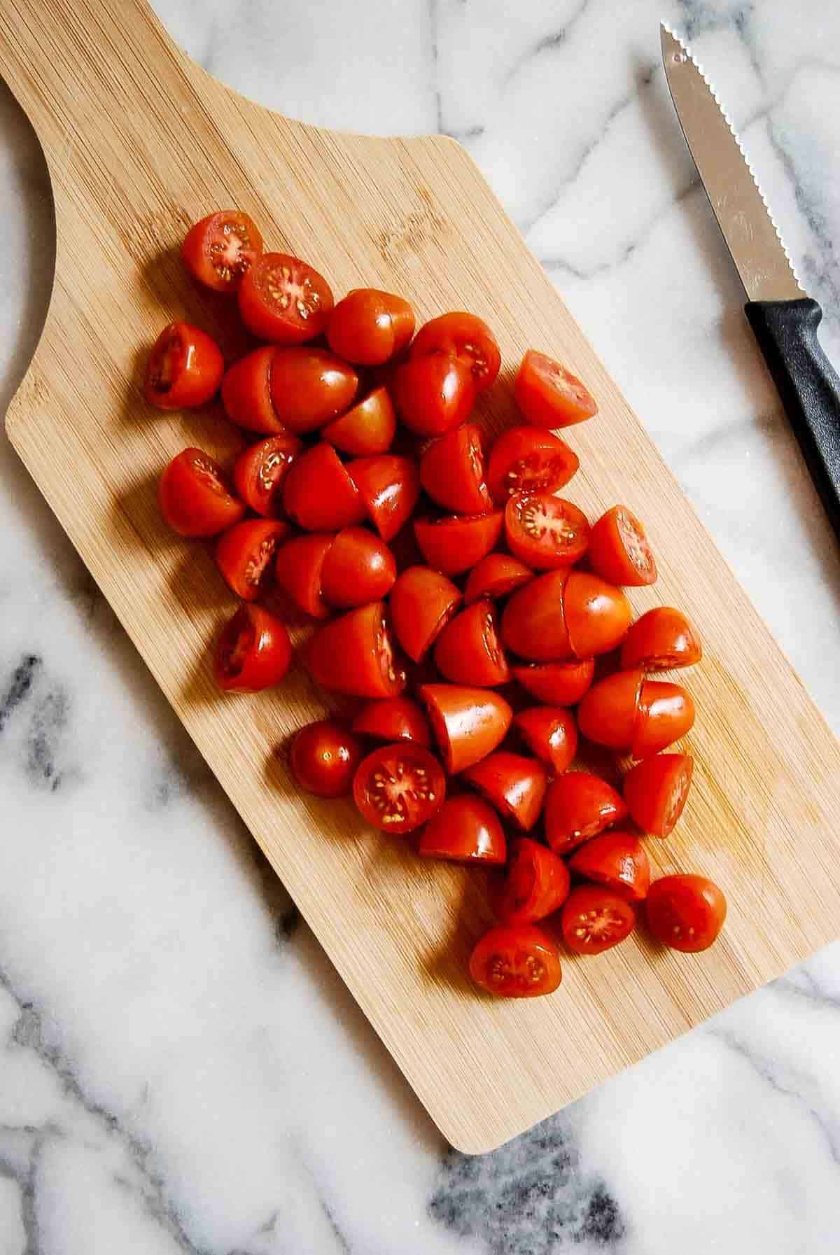 grape tomatoes, halved, on cutting board with knife on the side.