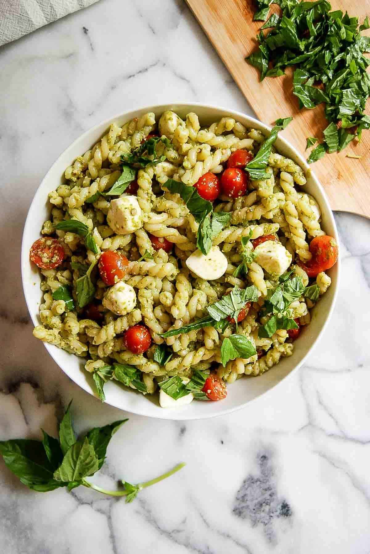 4-ingredient pesto pasta salad in serving bowl on countertop with basil sprinkled on top.