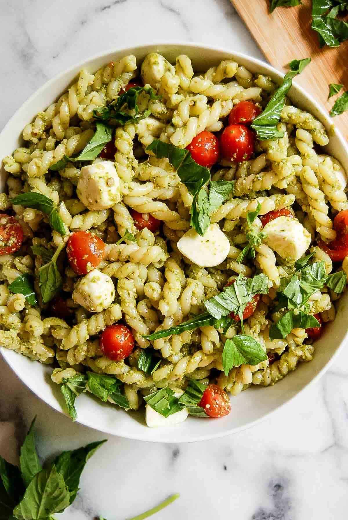4-ingredient pesto pasta salad in serving bowl on countertop with basil sprinkled on top.